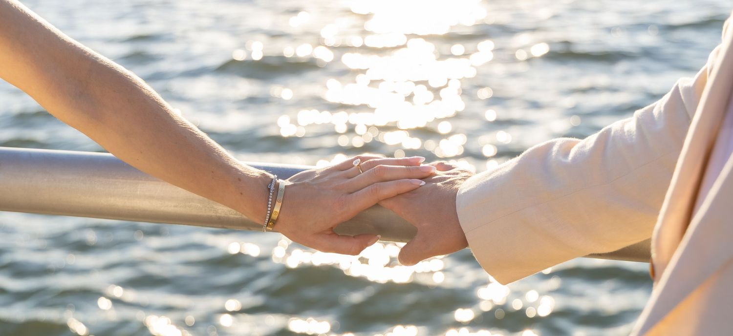 Two people holding hands near sparkling sunlit water, symbolizing love and connection.