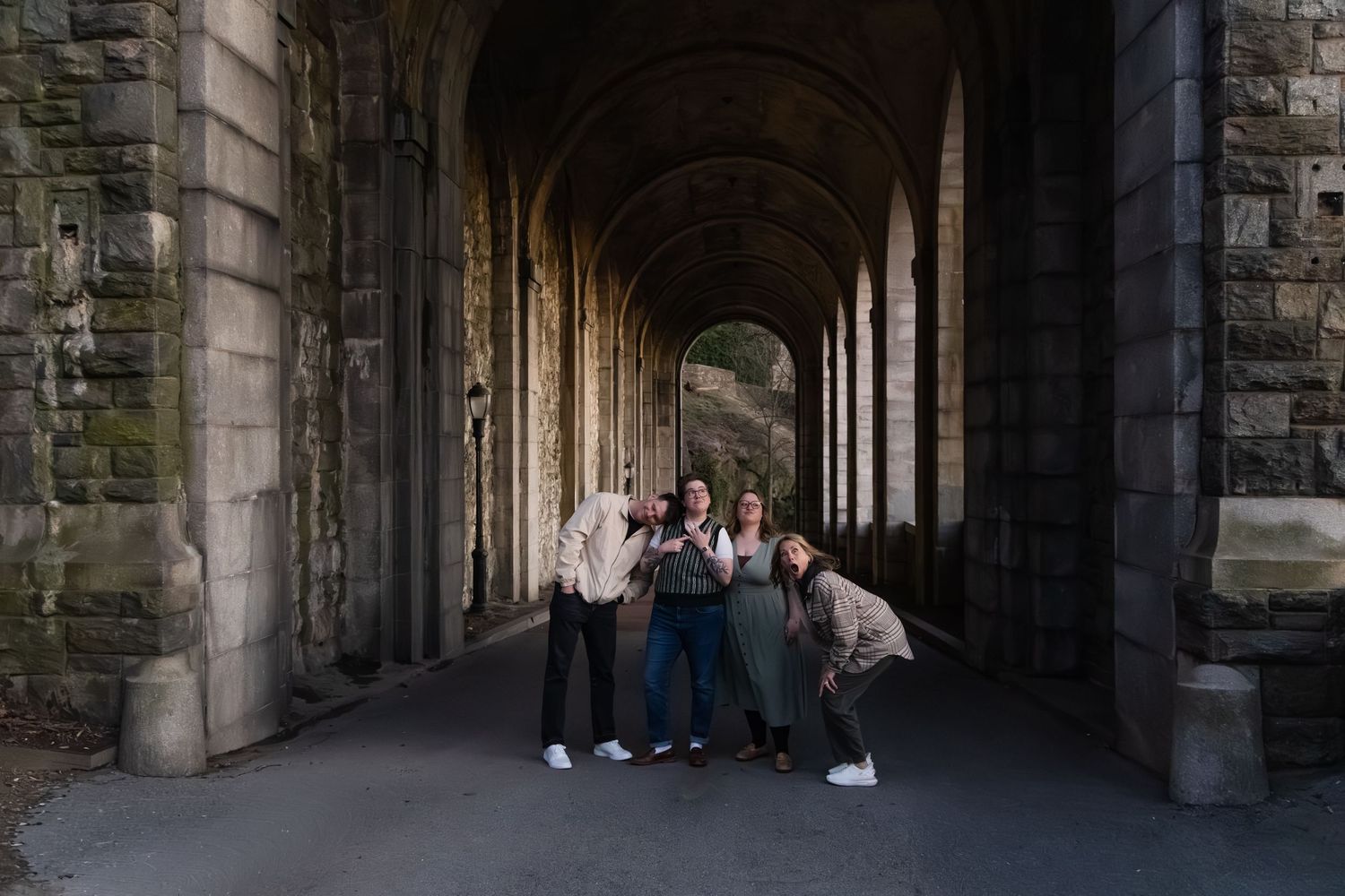 Four friends pose playfully under stone archway corridor with arched columns at historic castle.