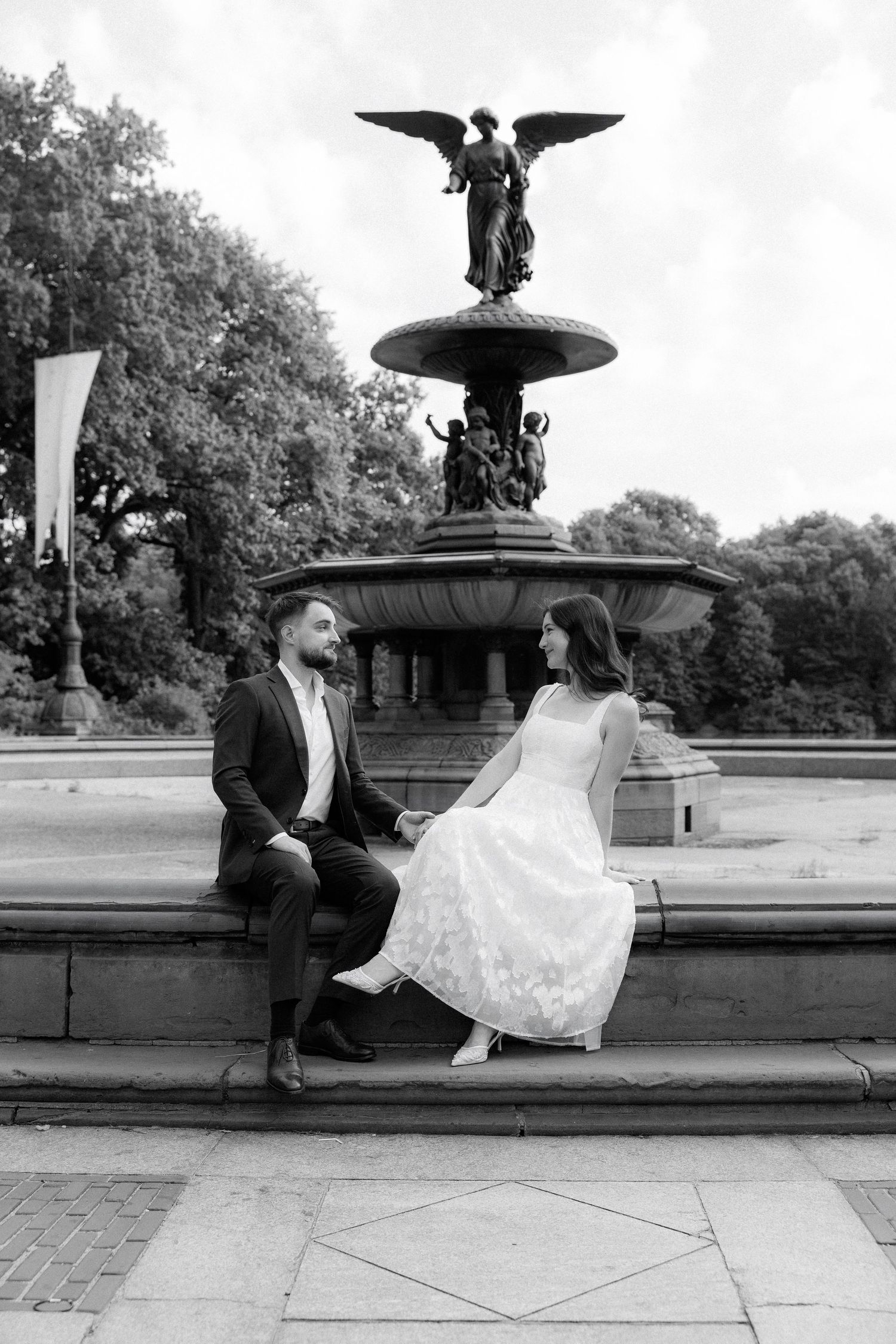 Couple in wedding attire holding hands at Bethesda Fountain in Central Park, black and white photo.