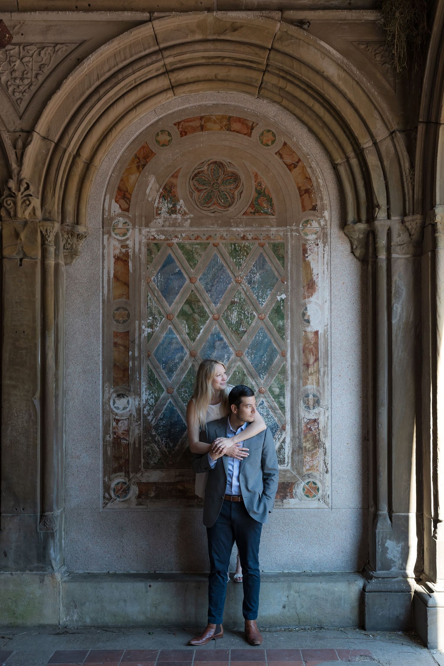 Couple embracing in a romantic stone archway with colorful mosaic tile artwork in Central Park NYC.
