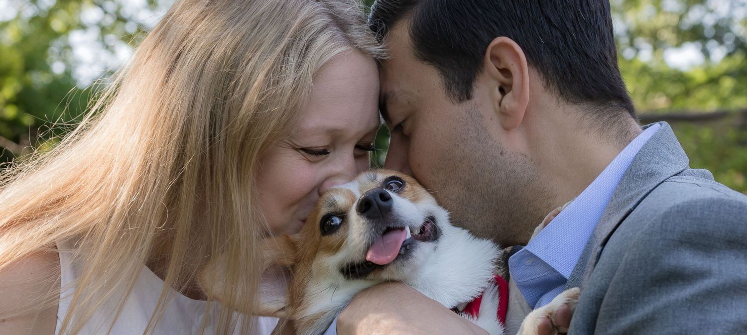 Happy couple sharing a tender moment with their smiling Corgi dog at an outdoor wedding celebration.