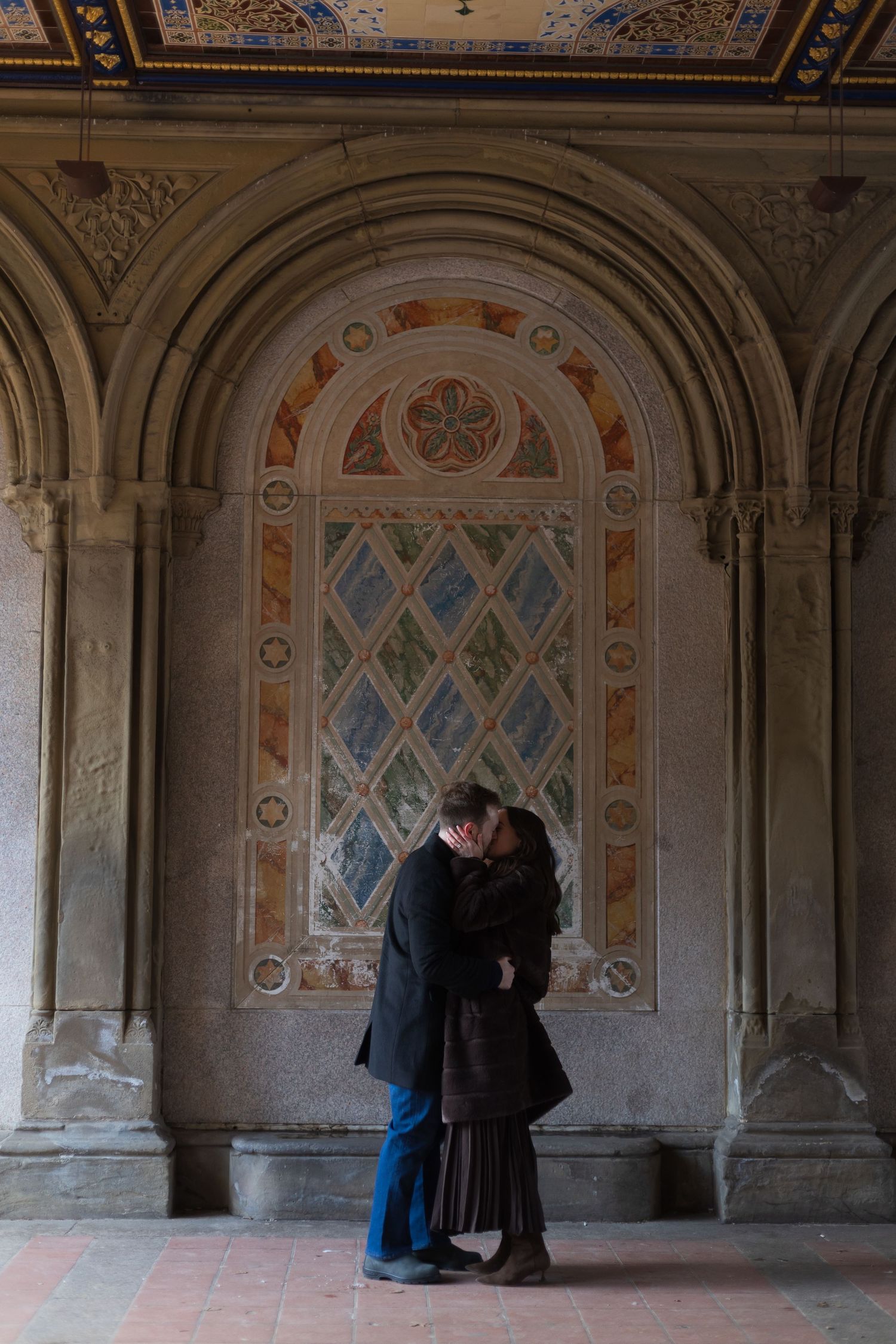 Romantic couple embracing under the Minton tiles at Bethesda Terrace in Central Park NYC soon after getting engaged.