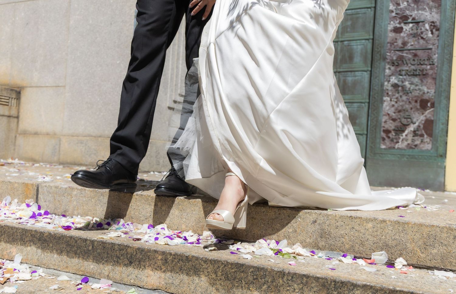 Close up of newlyweds' shoes as they walk out of the marriage bureau with confetti on the steps