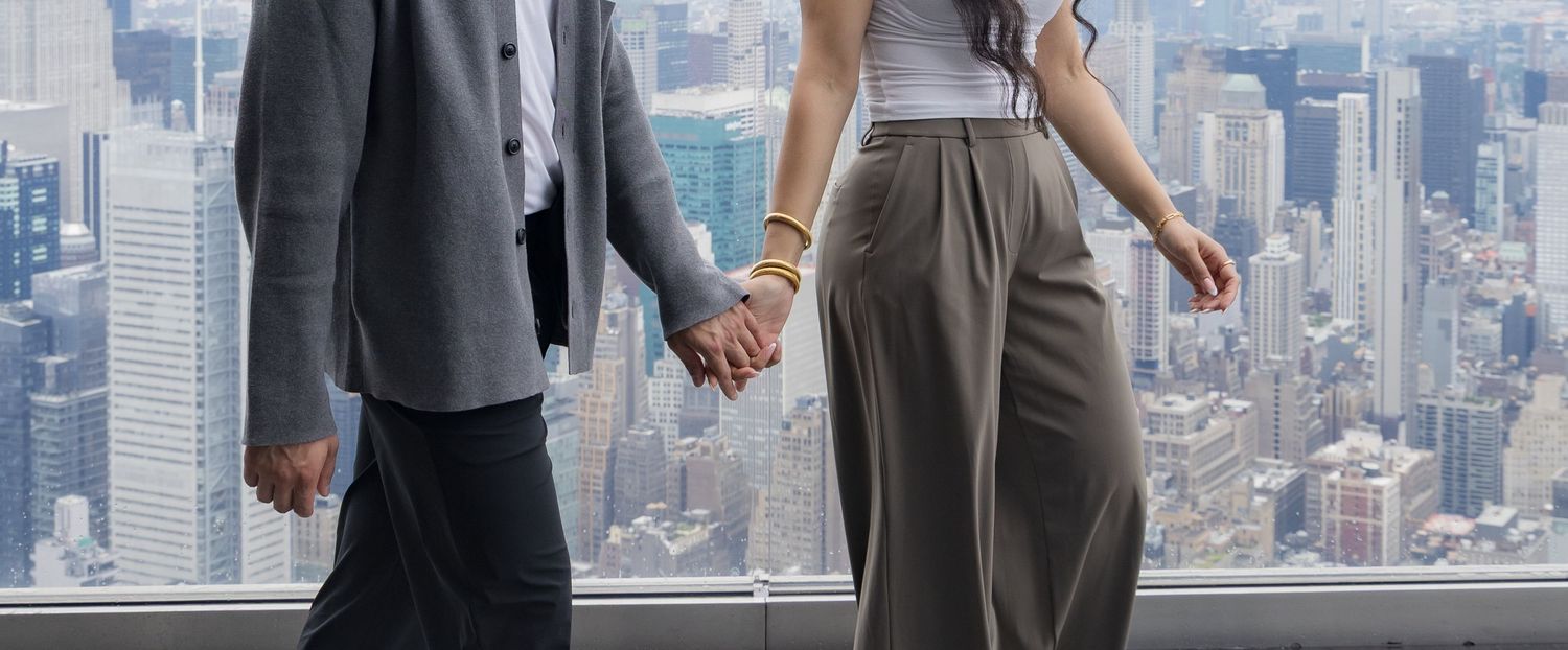 Couple holding hands at a skyscraper observation deck overlooking a city skyline.