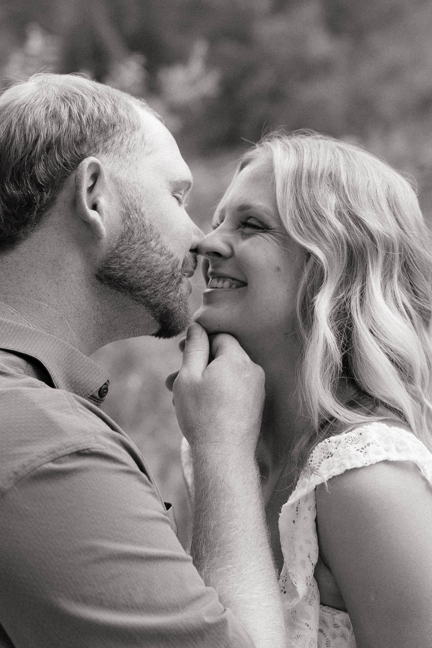 Black and white photo of a smiling couple sharing a tender moment, man gently holding womans face as they lean close.