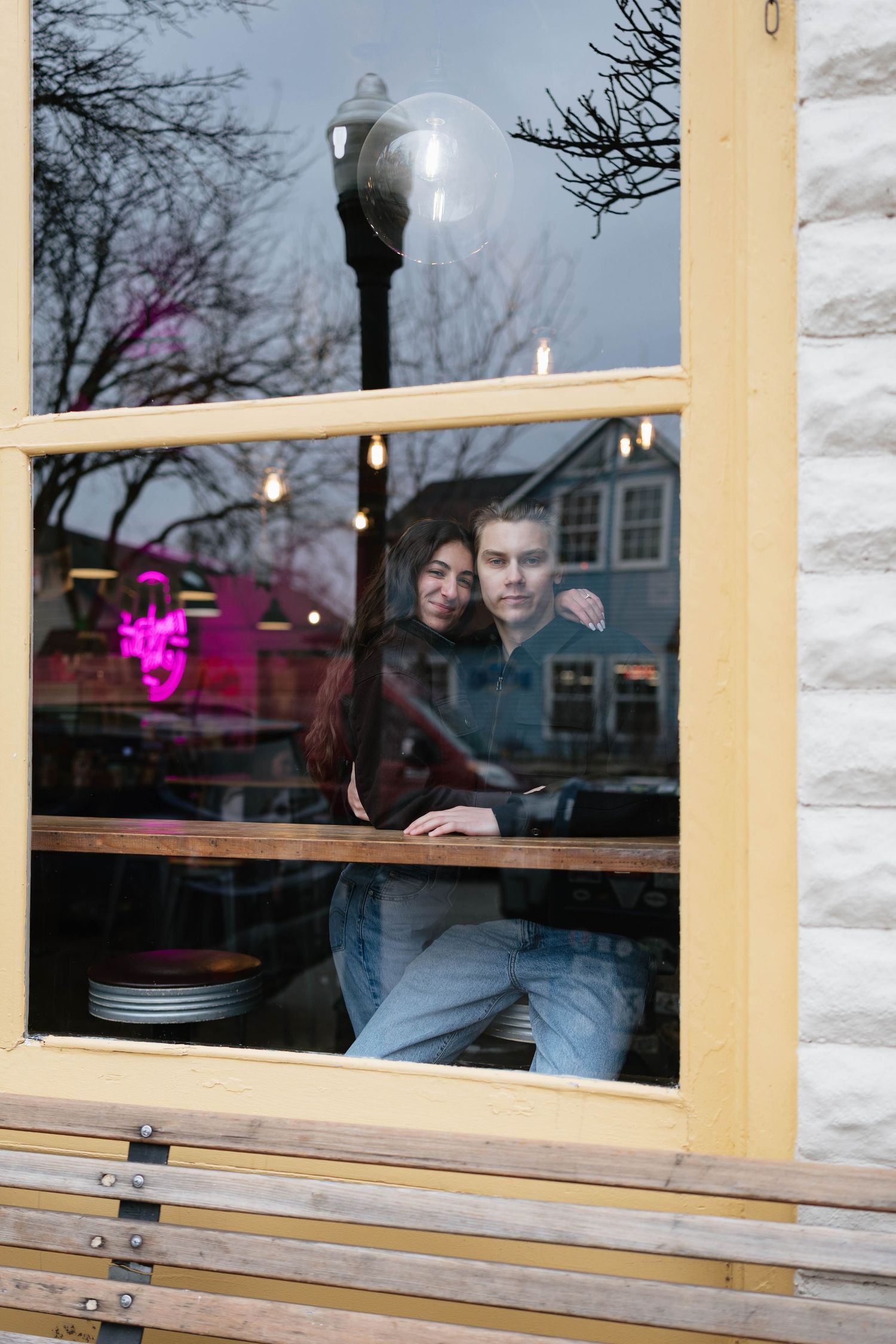 Couple sits together in a cozy restaurant window booth with yellow trim and white stone exterior.