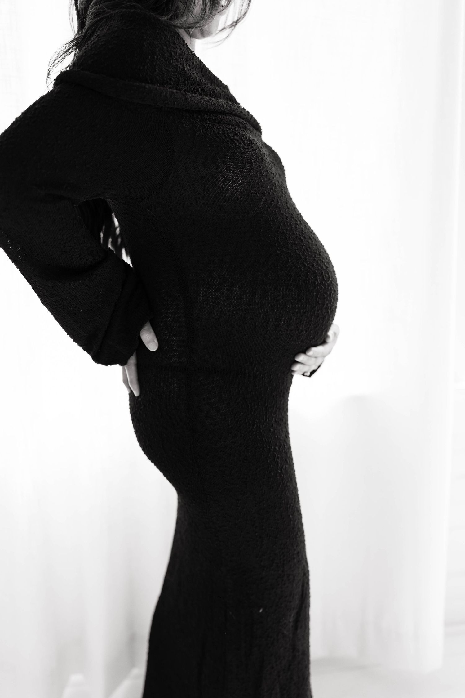 Black and white photo of a pregnant woman in a black knit dress cradling her baby bump.