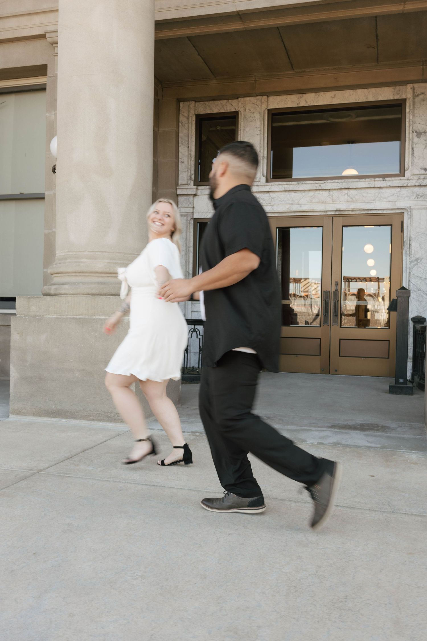 Two people in black and white outfits dance together in front of a building entrance with columns.