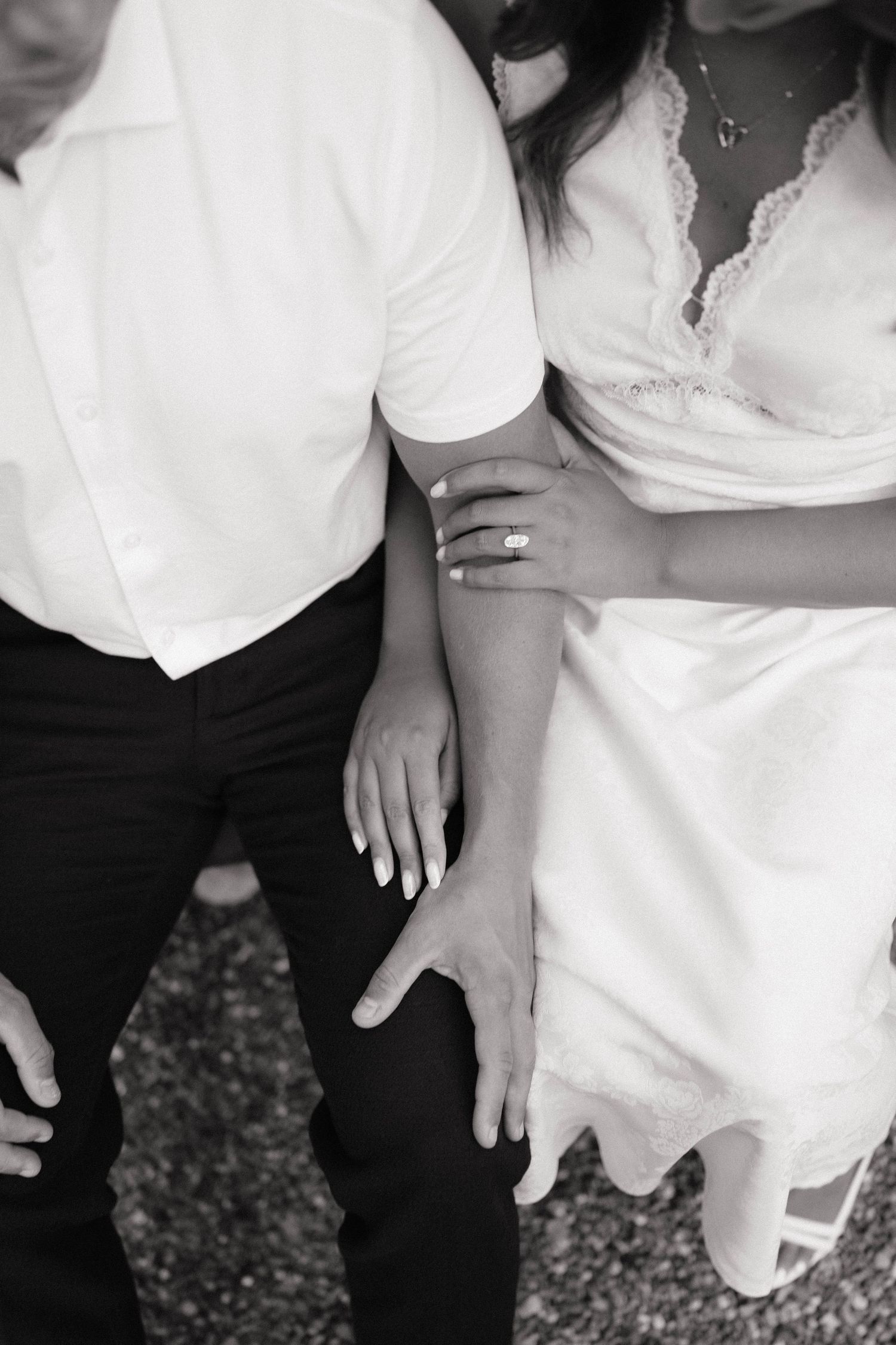 Black and white photo of a couple holding hands, bride in white dress with engagement ring visible.