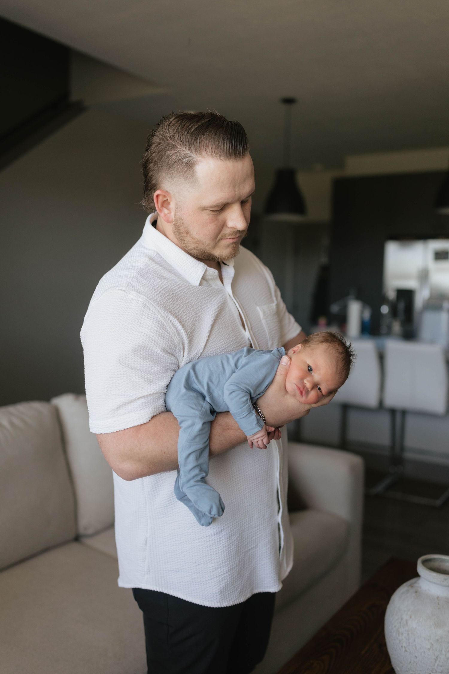 A person in a white shirt holds a small baby wearing light blue clothing in a modern living room interior.