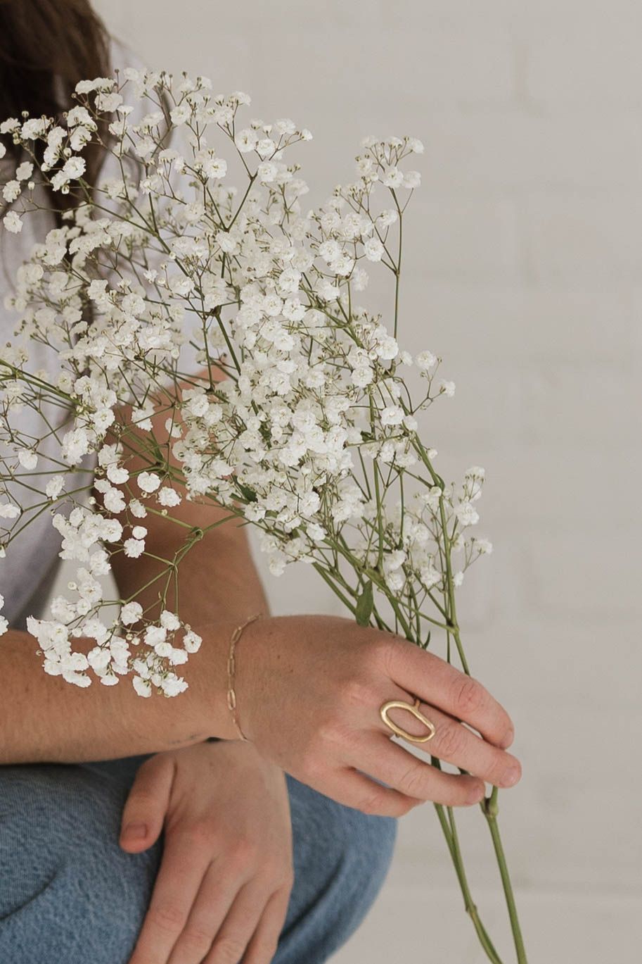 Close-up of hands holding delicate white baby's breath flowers against a light background.