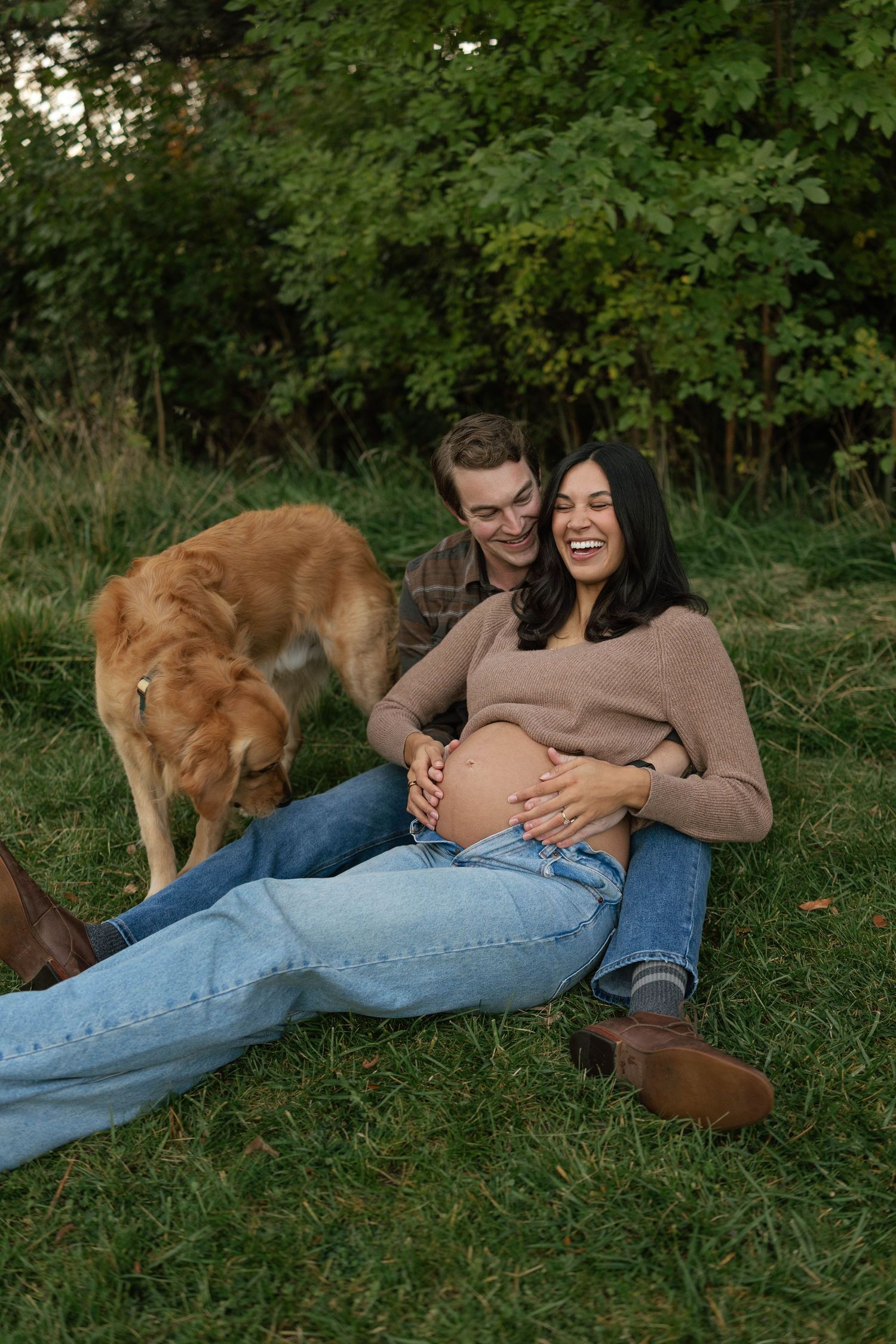 A couple relaxes on grass with their golden retriever dog in a series of candid outdoor autumn photos.