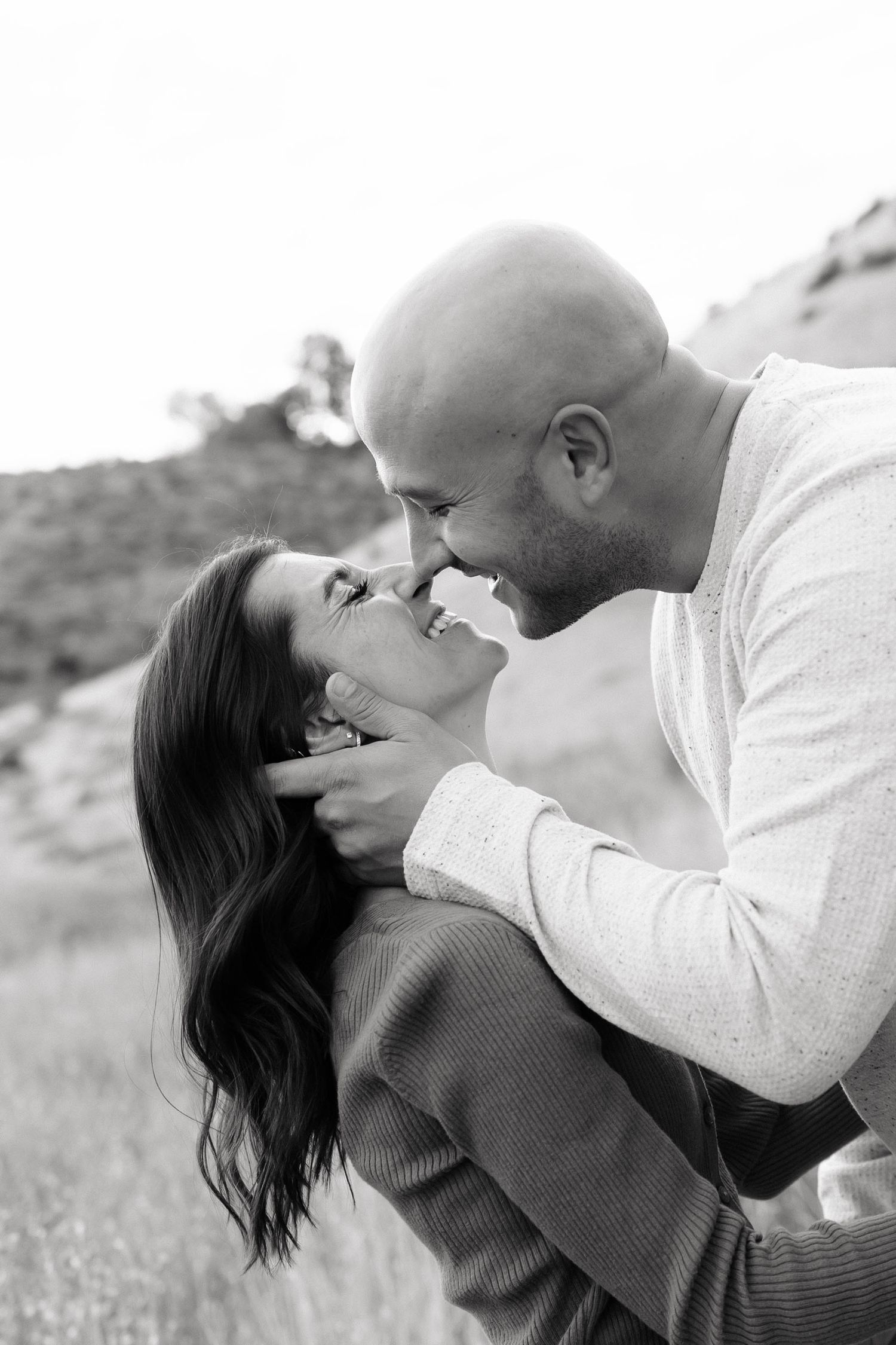 A romantic couple embraces and kisses in a black and white outdoor portrait series.