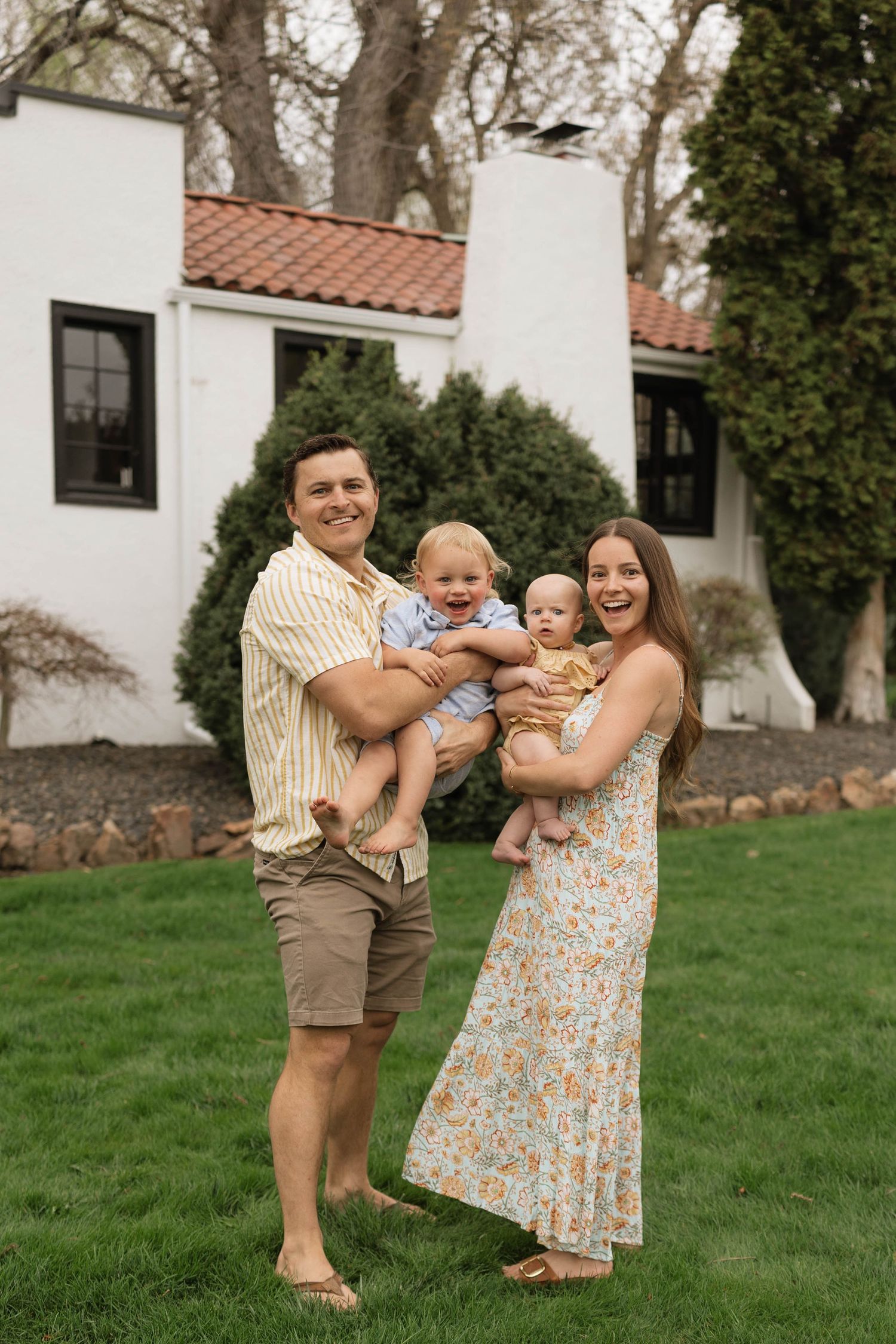 A family shares joyful moments together on a grassy lawn outside a white Spanish-style building.