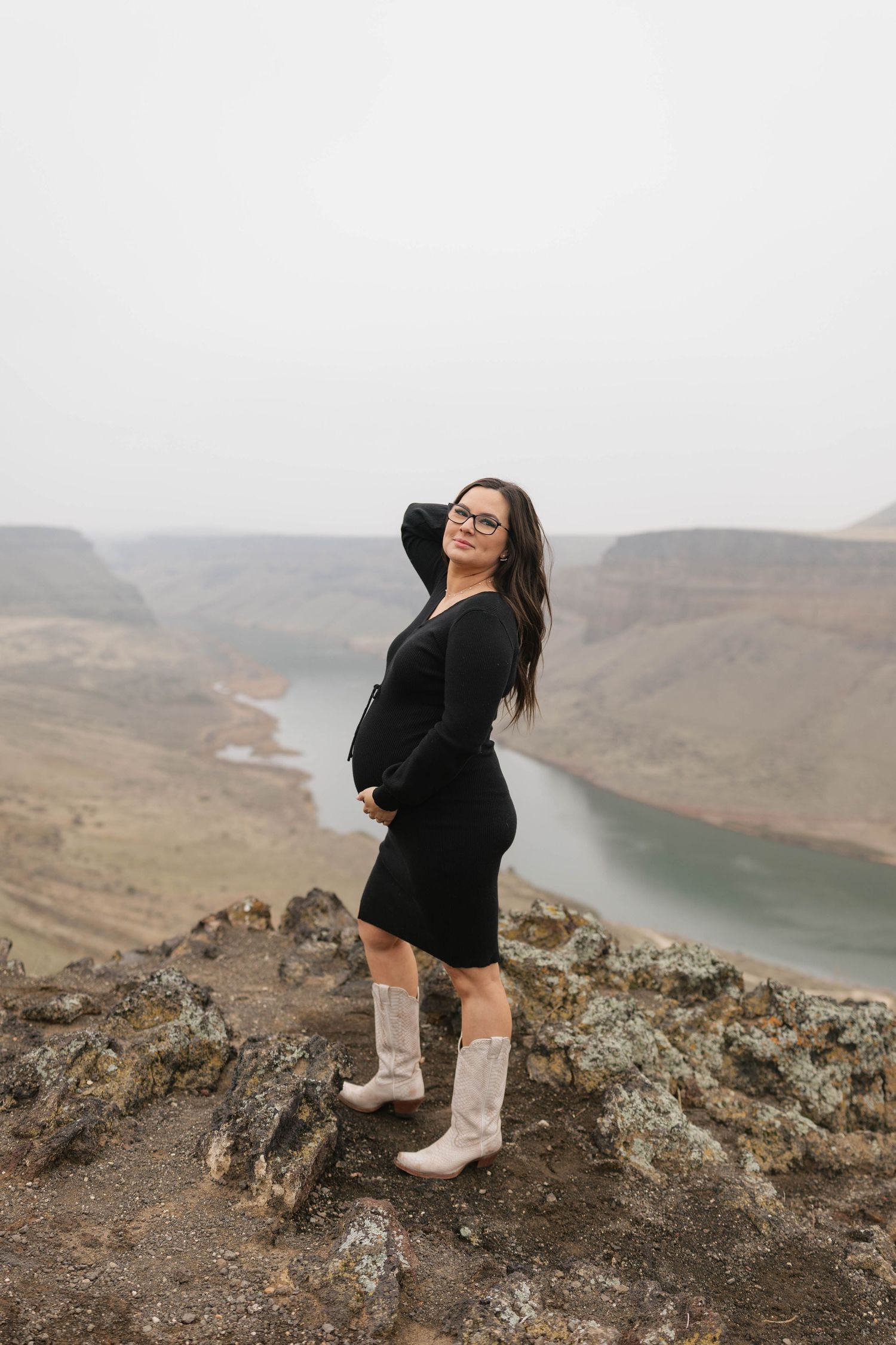 A person in black clothing and boots explores a rocky mountain ridge overlooking a scenic lake and rugged landscape.