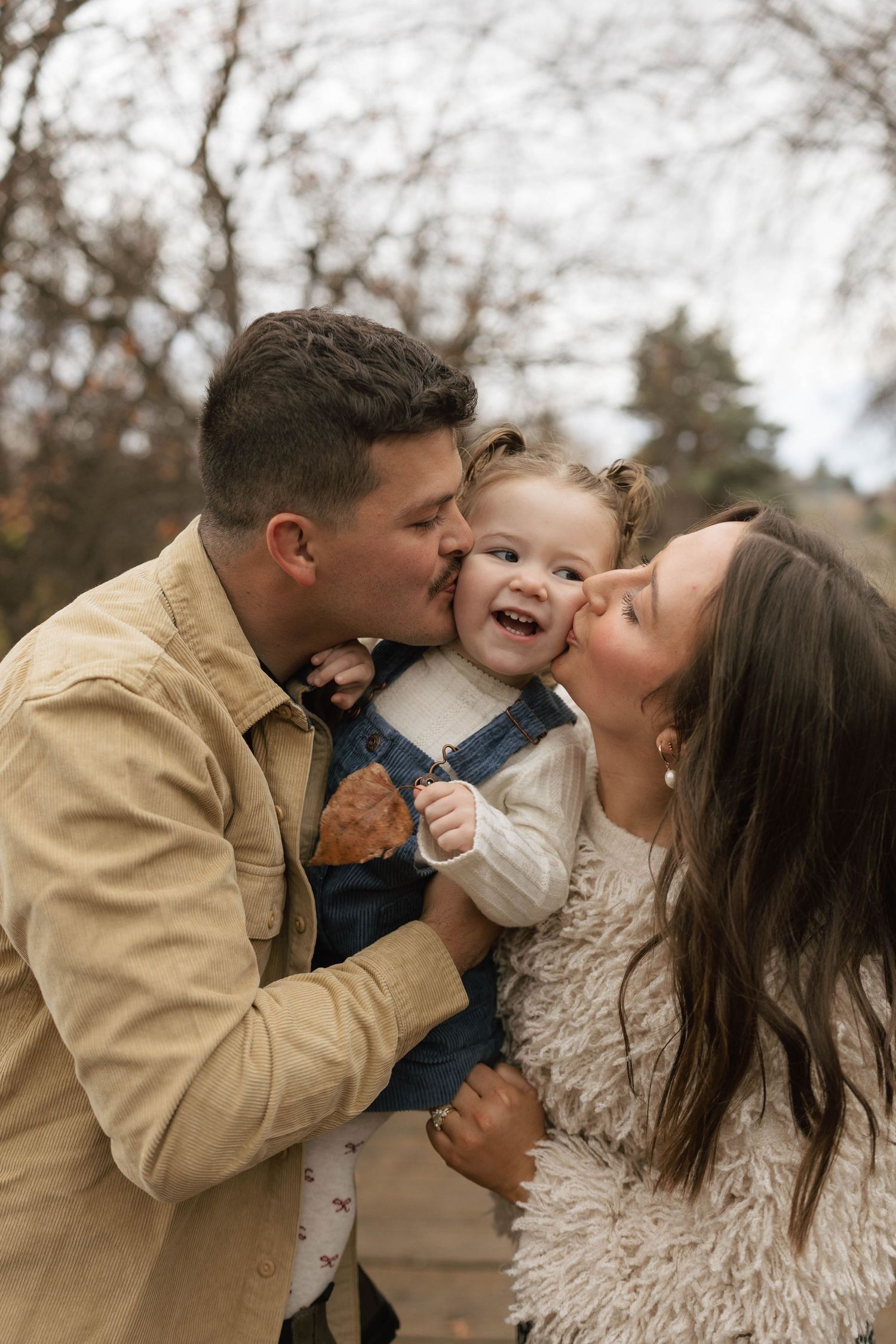 A loving family shares playful kisses and laughter together during an outdoor photo session in autumn.
