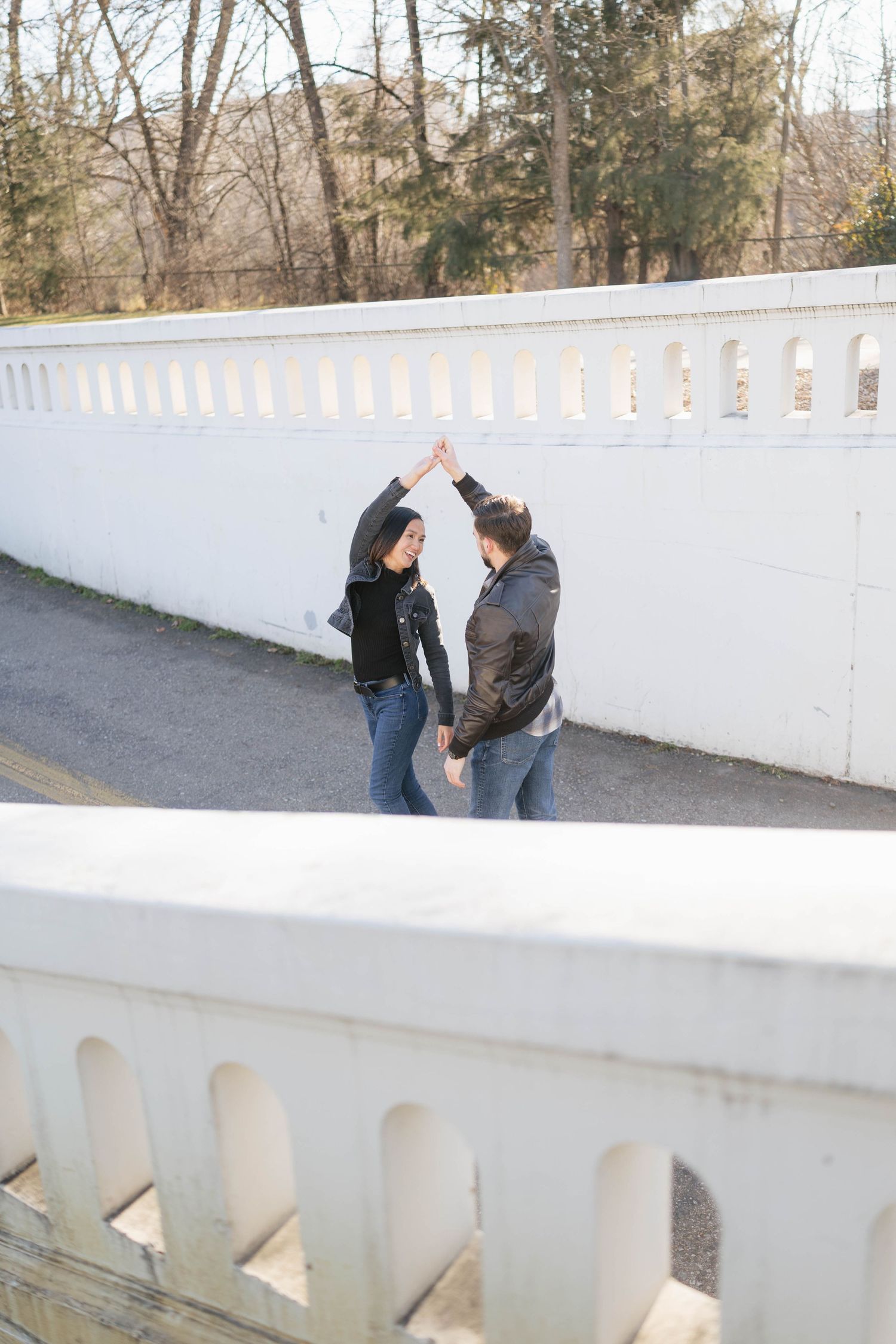 Two people lean against a white concrete bridge railing while having a conversation on a sunny day.