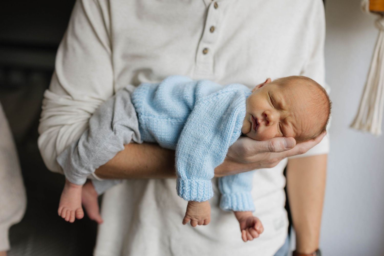 Gentle cradling of infant wearing soft blue clothing against white background.
