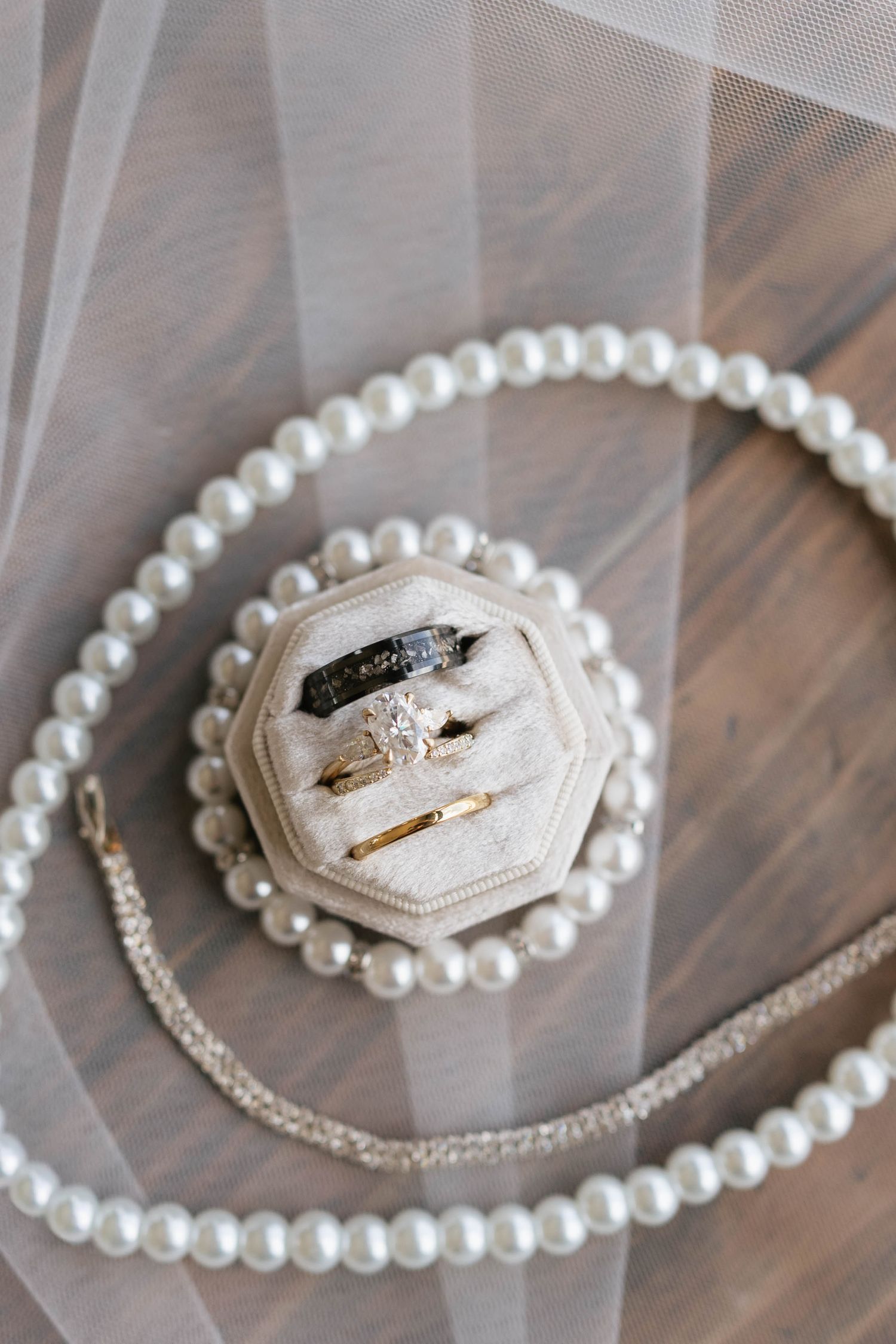 Elegant wedding rings displayed in a velvet octagonal box surrounded by a pearl necklace on a wooden surface.
