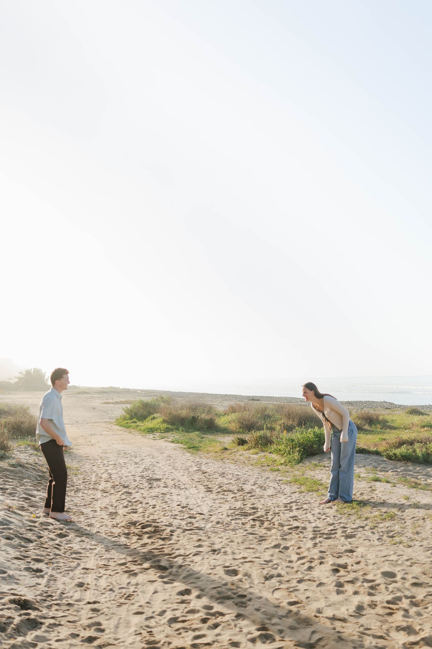 People enjoying a sunny day on a sandy beach with coastal vegetation visible in the background.
