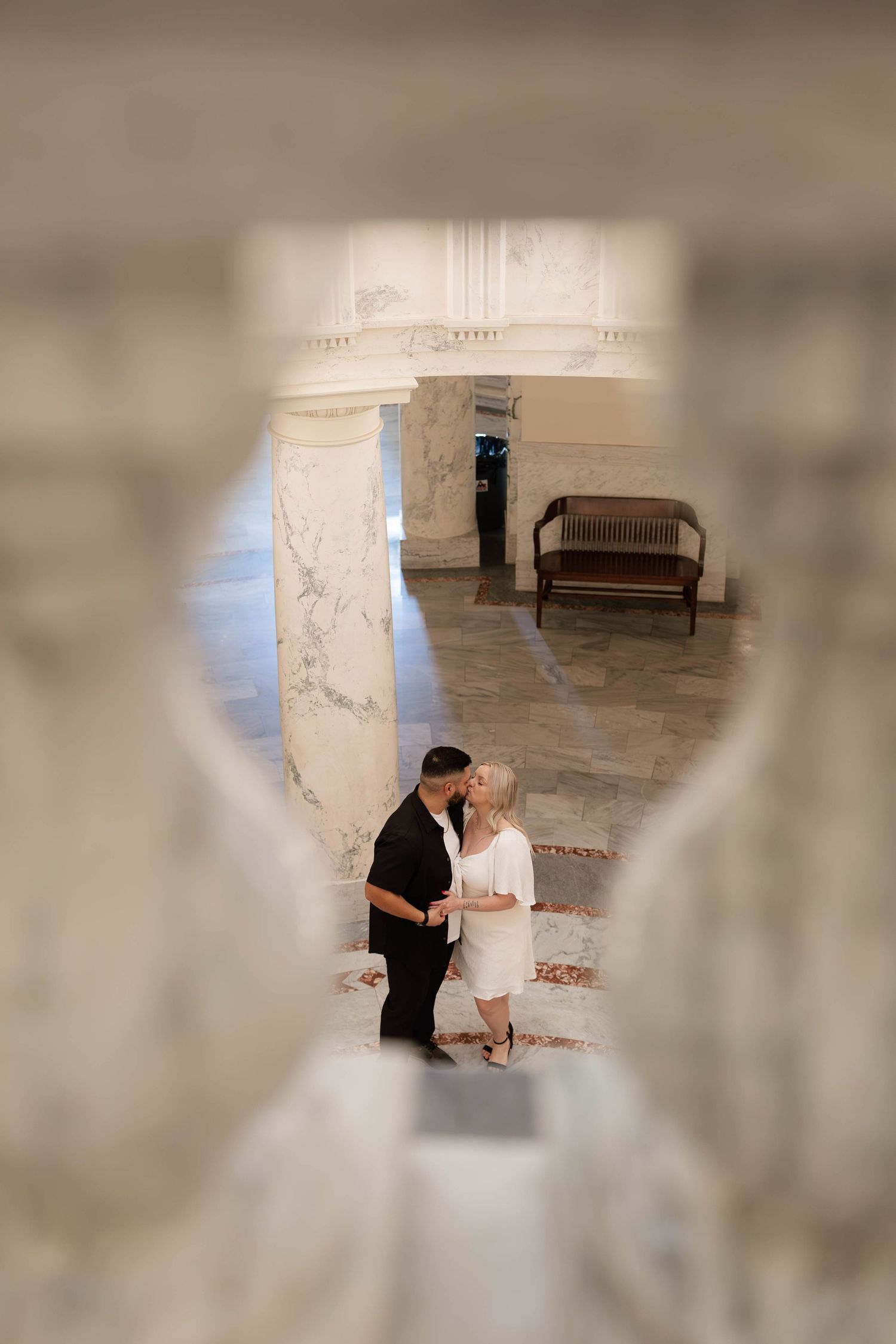 A couple shares an intimate moment in a rustic stone hallway with white walls and natural lighting.