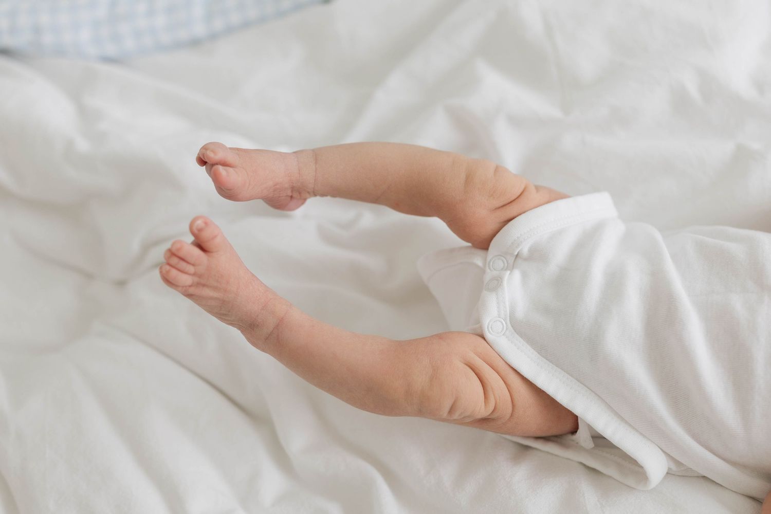 Tiny baby feet and legs resting on soft white bedding.