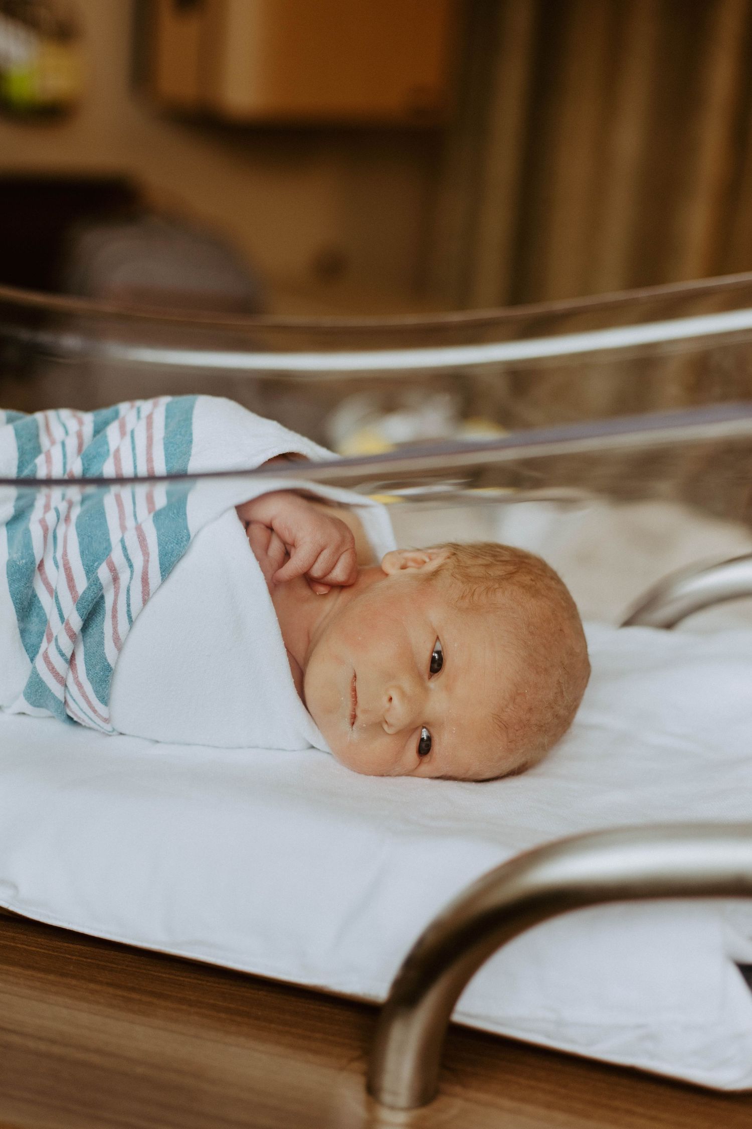 Newborn baby swaddled in white and blue striped blanket lying on hospital bassinet.
