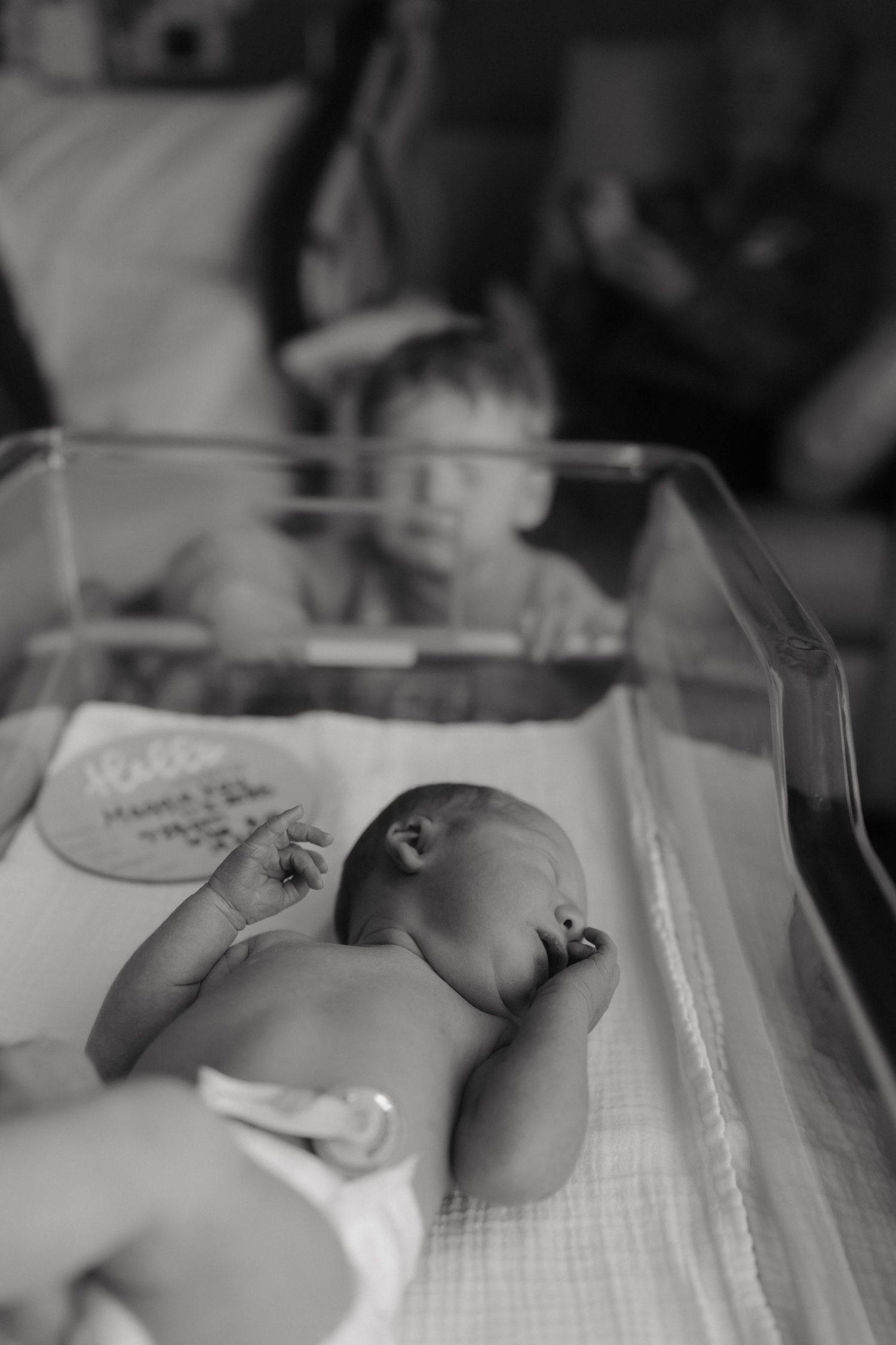 Black and white image of a newborn baby resting in a hospital bassinet.