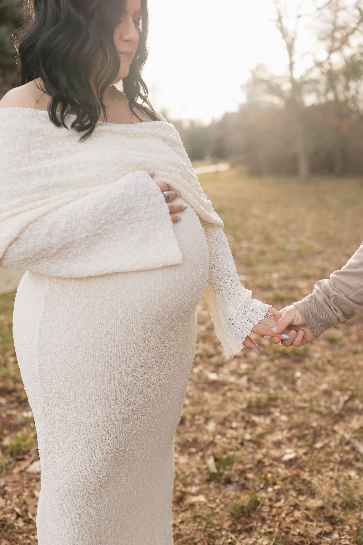A person wearing a cozy cream-colored blanket wrap stands in a sunlit autumn field with fallen leaves.
