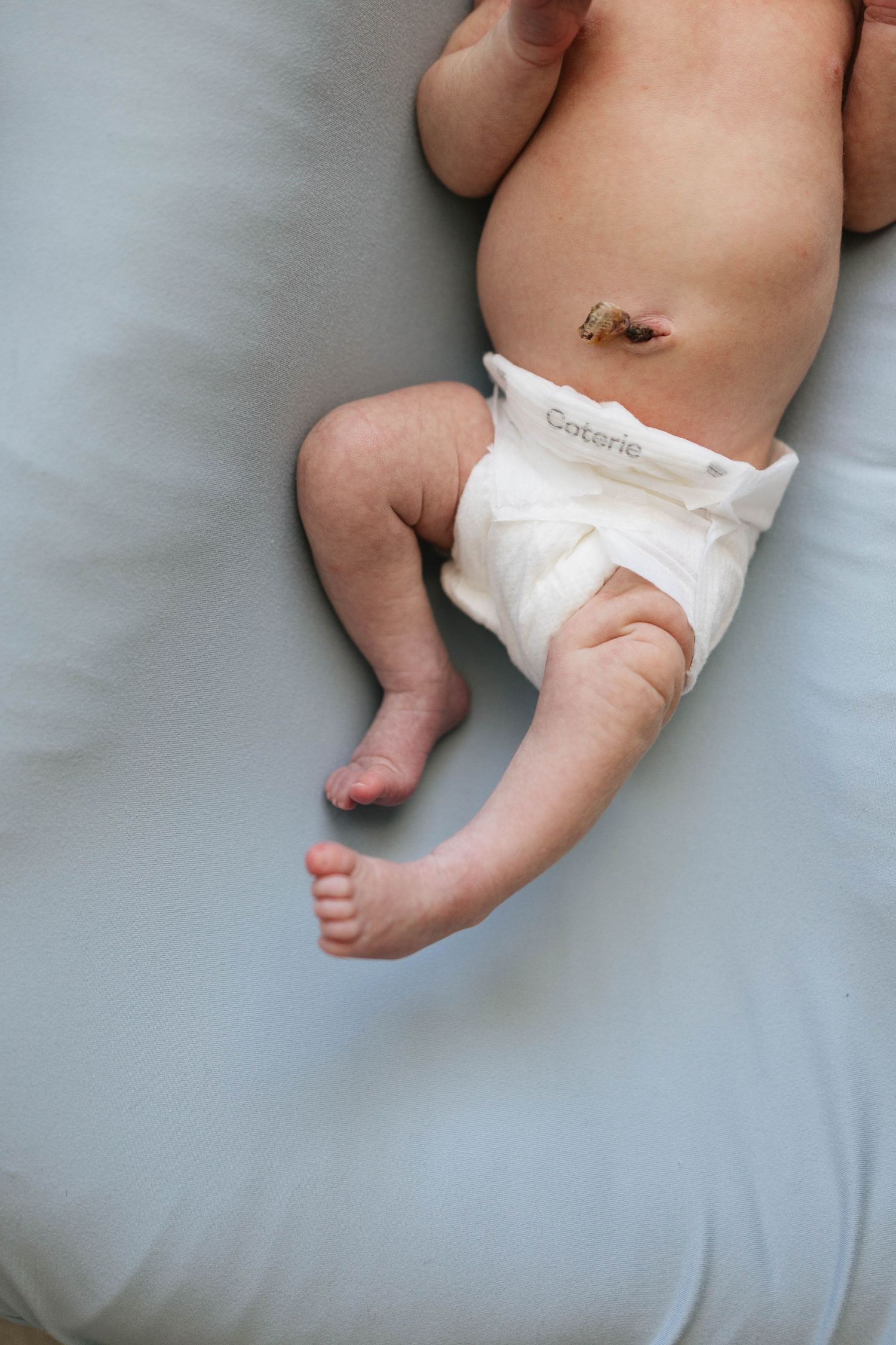 Close-up view of baby's tiny feet and diaper against soft gray bedding.