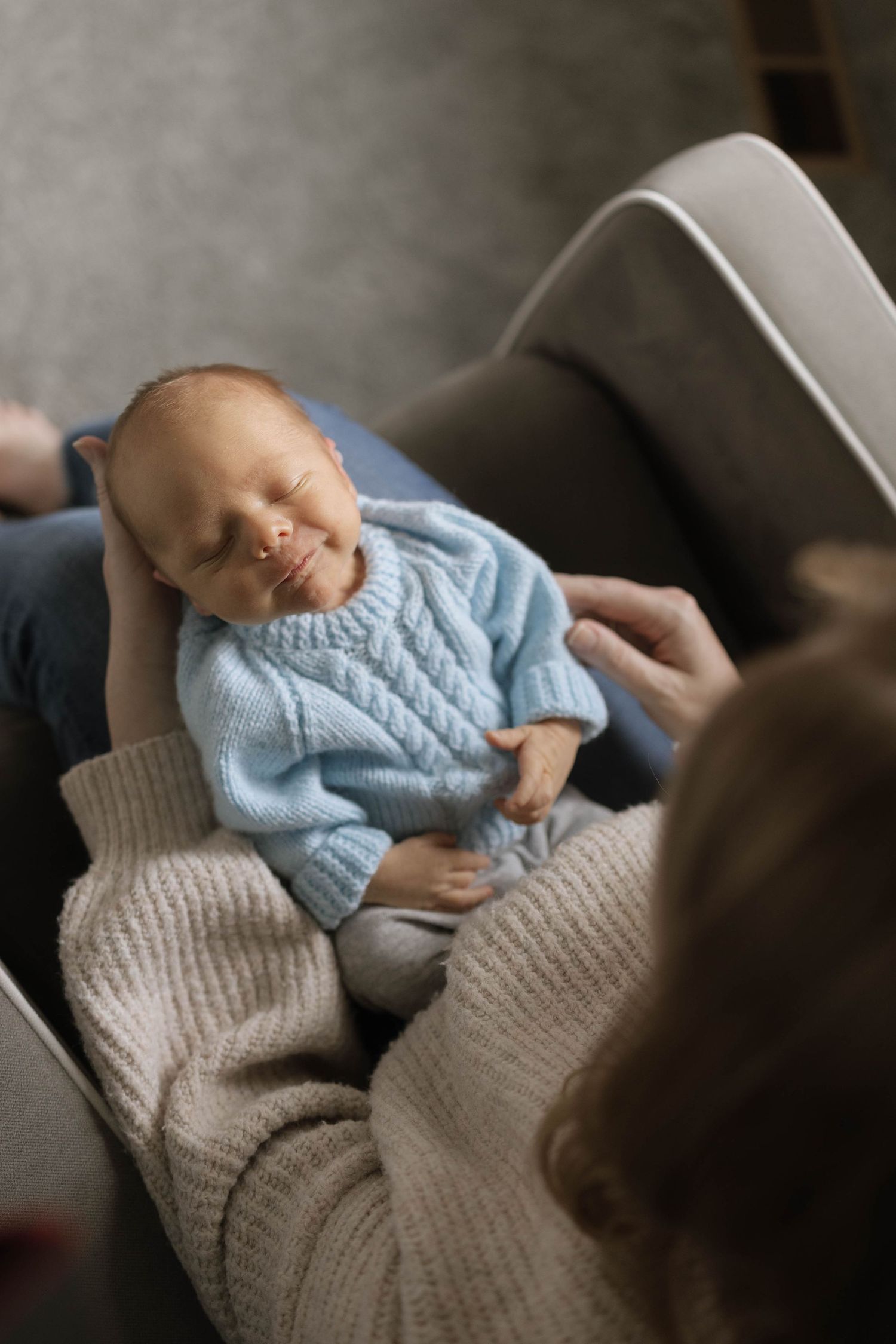 Baby wearing light blue sweater resting peacefully on a textured grey blanket.