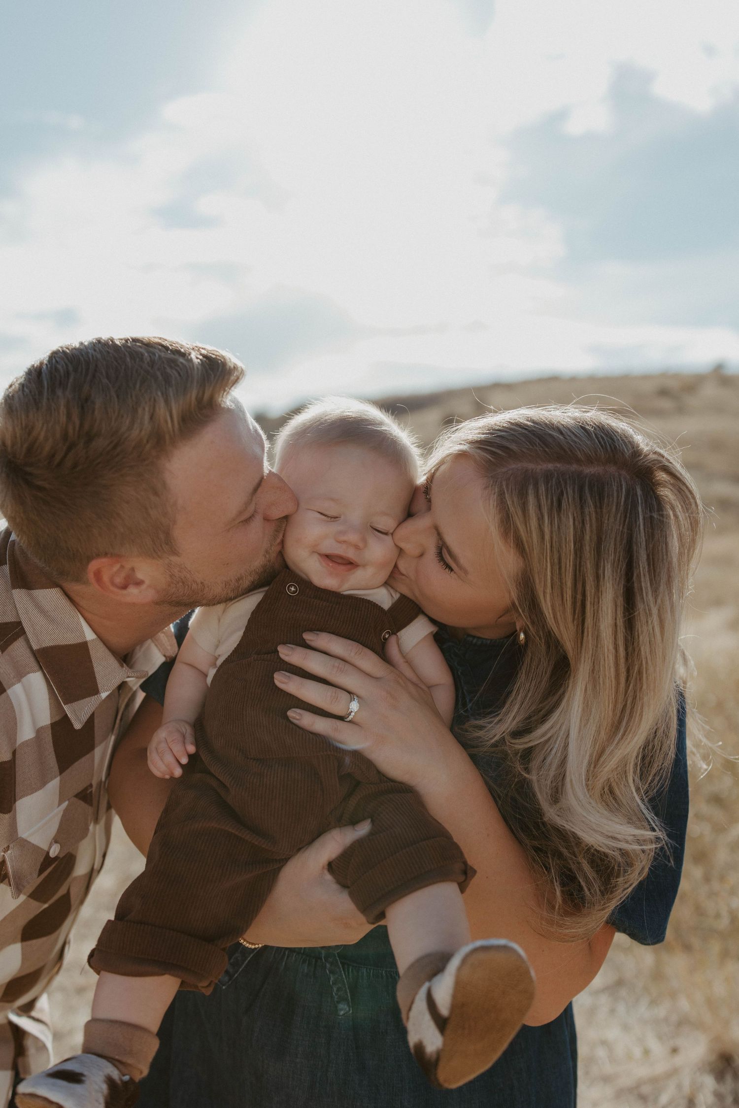 A loving family shares sweet kisses together against a bright outdoor backdrop.