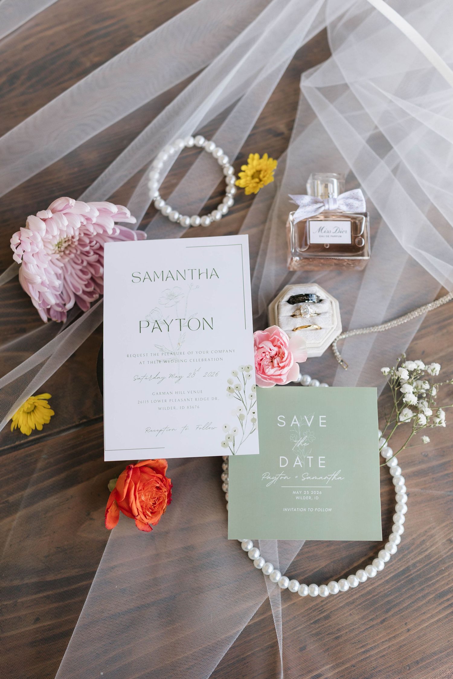 Wedding flat lay with floral invitation, save the date card, pearl jewelry, perfume bottle, and colorful flowers on tulle.