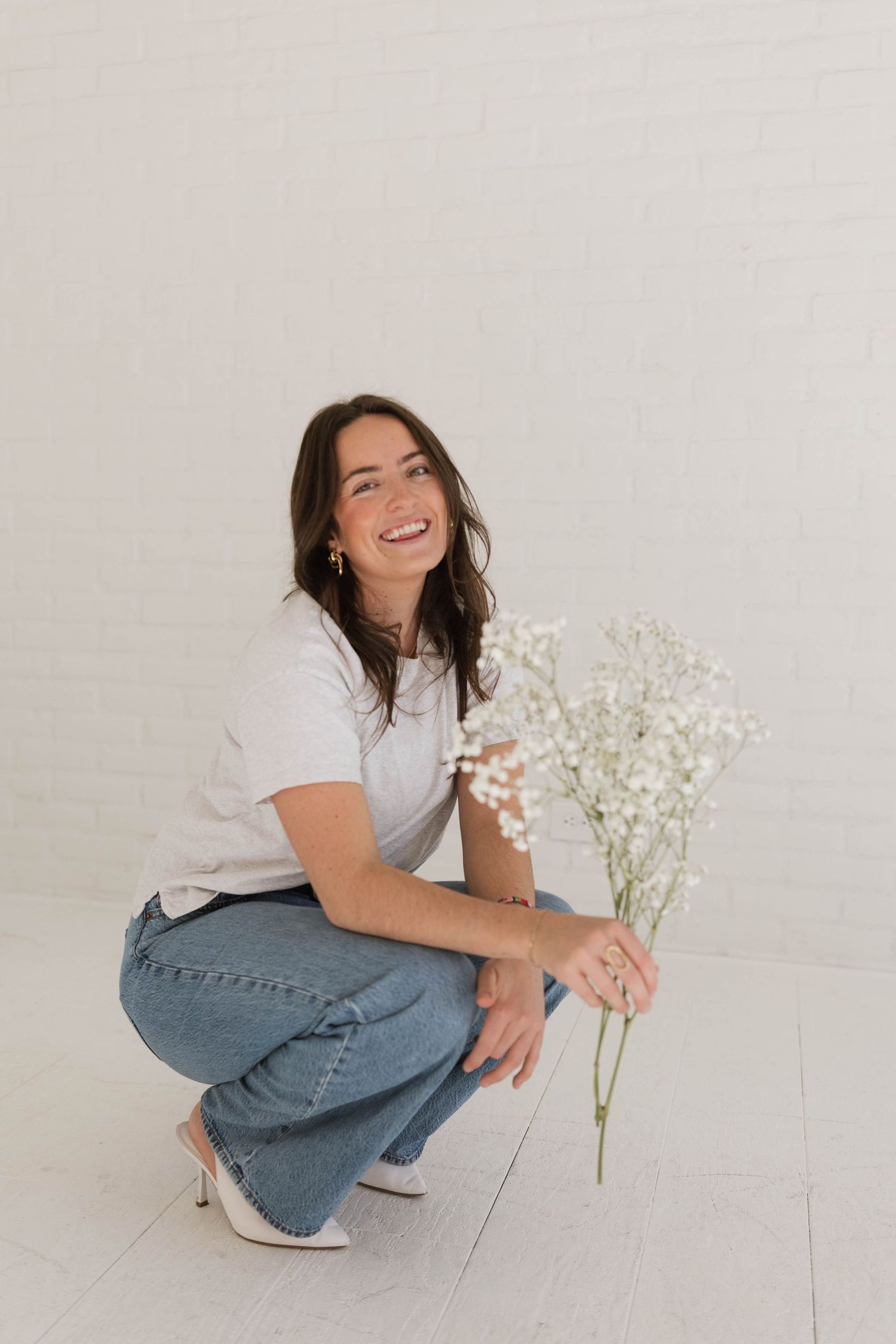 Person in casual denim and white shirt posing playfully with baby's breath flowers on white floor.
