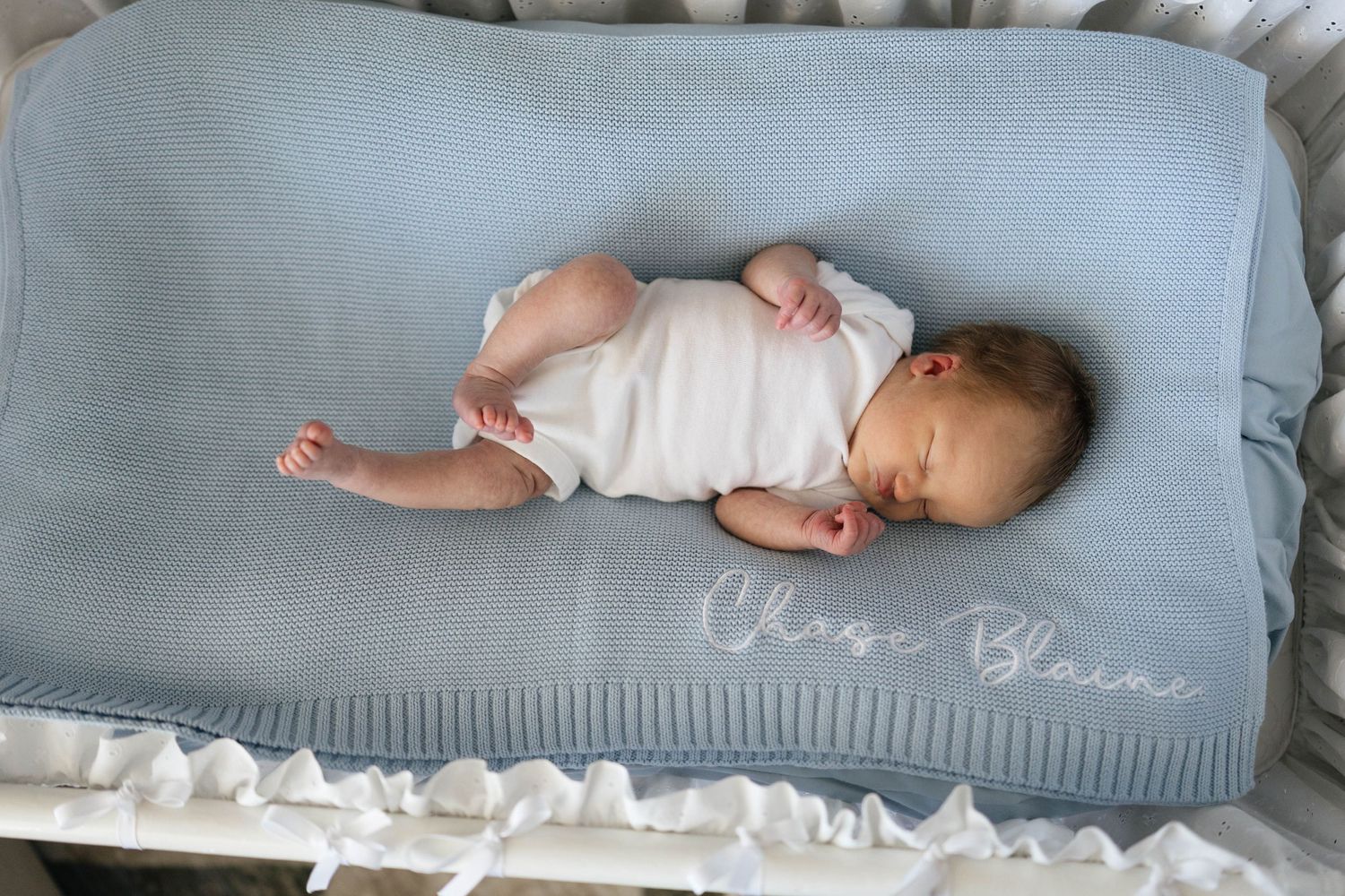 A baby lies peacefully sleeping on a gray couch with white tissue papers scattered around.