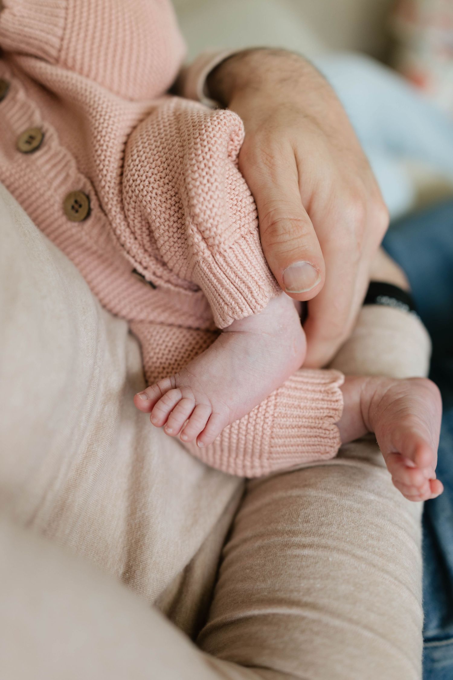 Close-up of a newborn baby in a pink knit outfit being cradled in an adult's hands.