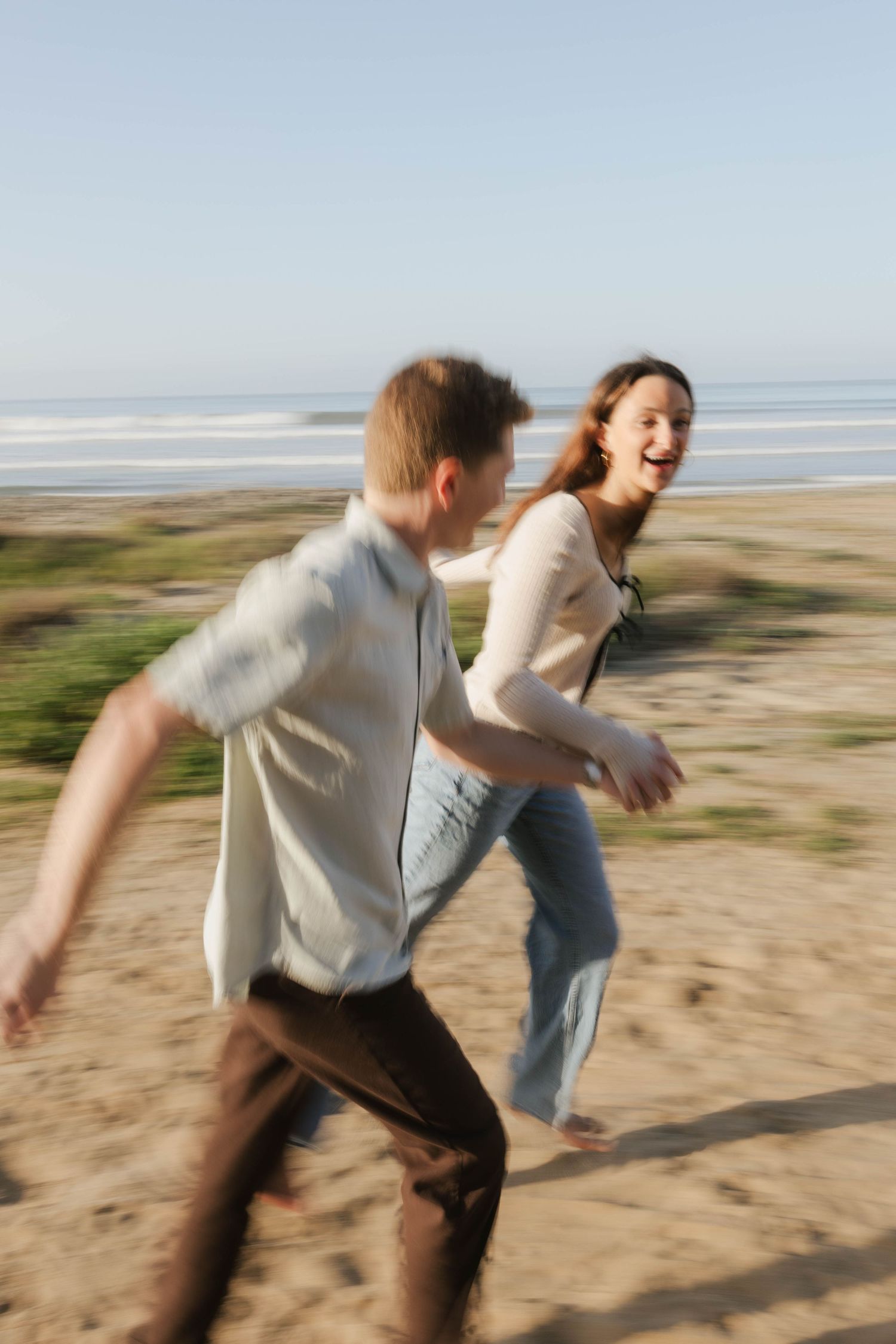 Motion blur captures two people running playfully along a sandy beach with ocean waves in the background.