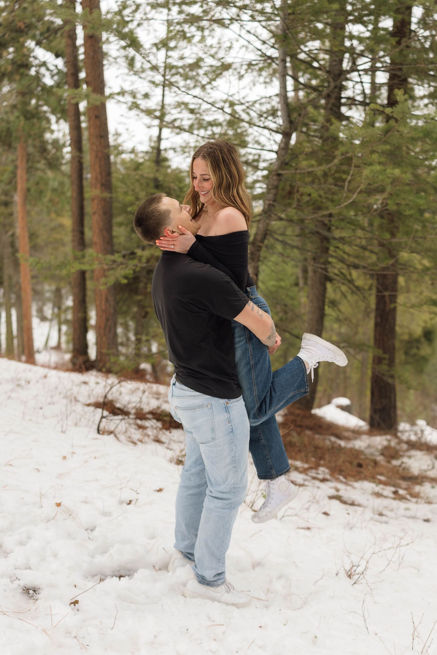 Playful couple shares intimate moments while posing in the snow-covered woods.