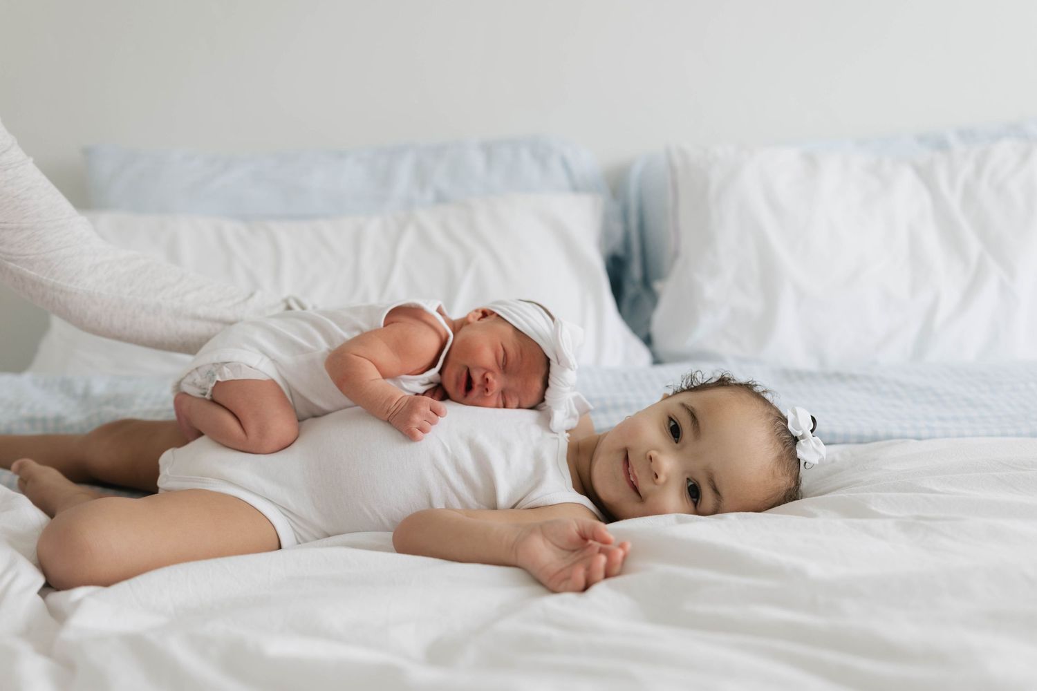 A sleeping baby lies peacefully on white bedding in a soft, natural light setting.