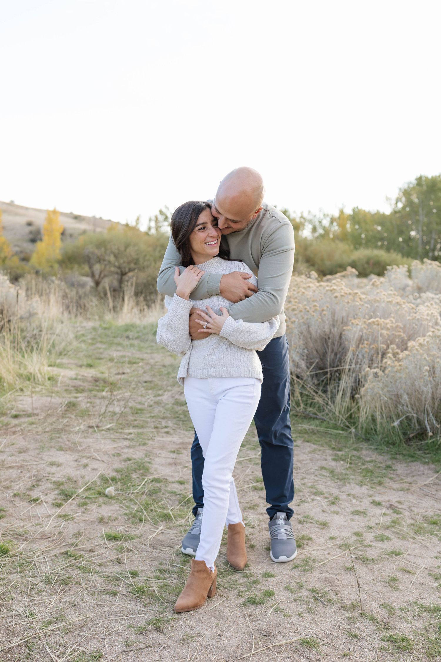 Romantic couple embraces in a desert landscape with dry brush and golden sunlight.