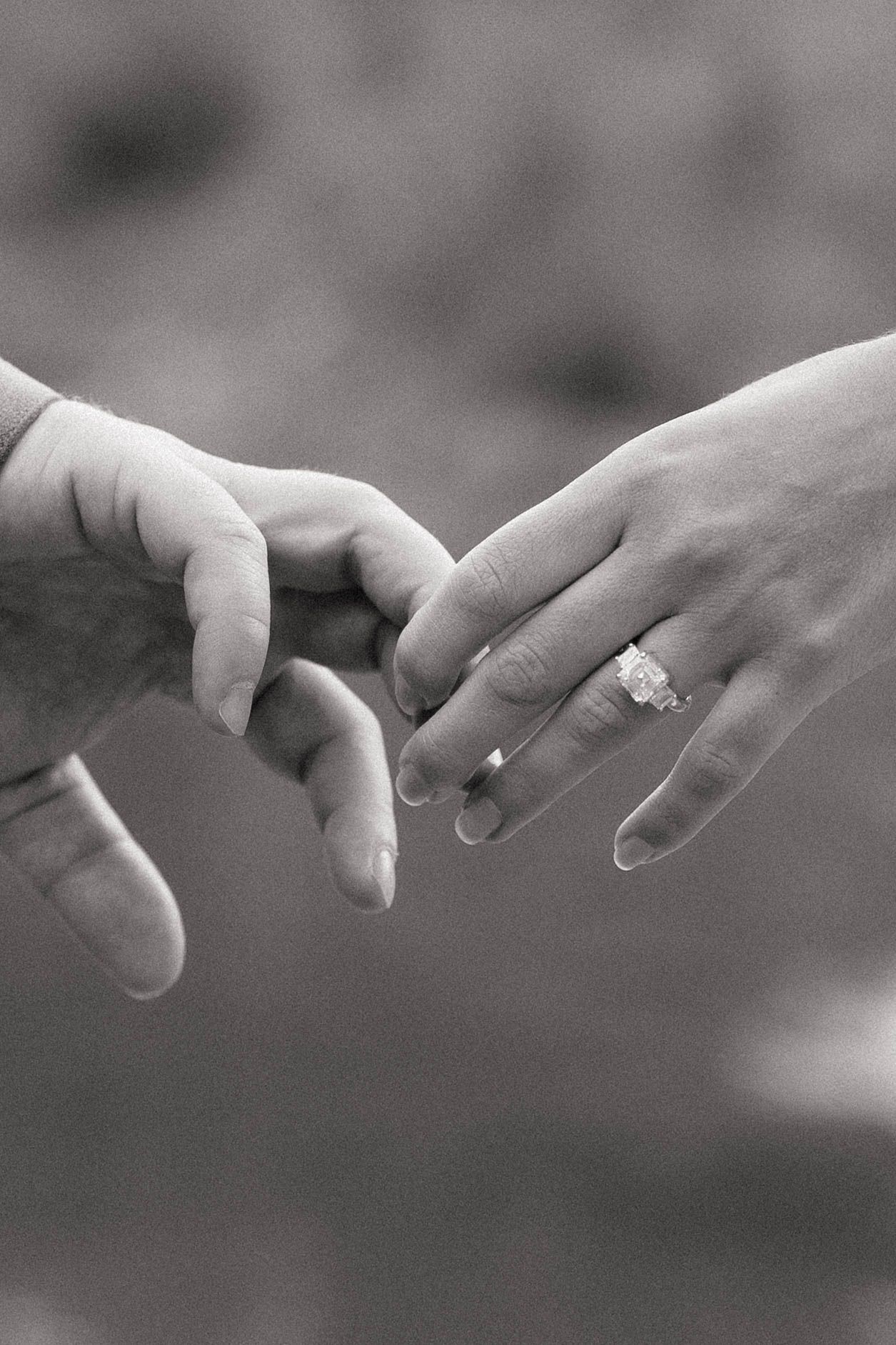 Black and white photo of two hands gently touching, with a sparkling diamond engagement ring on the woman's finger.