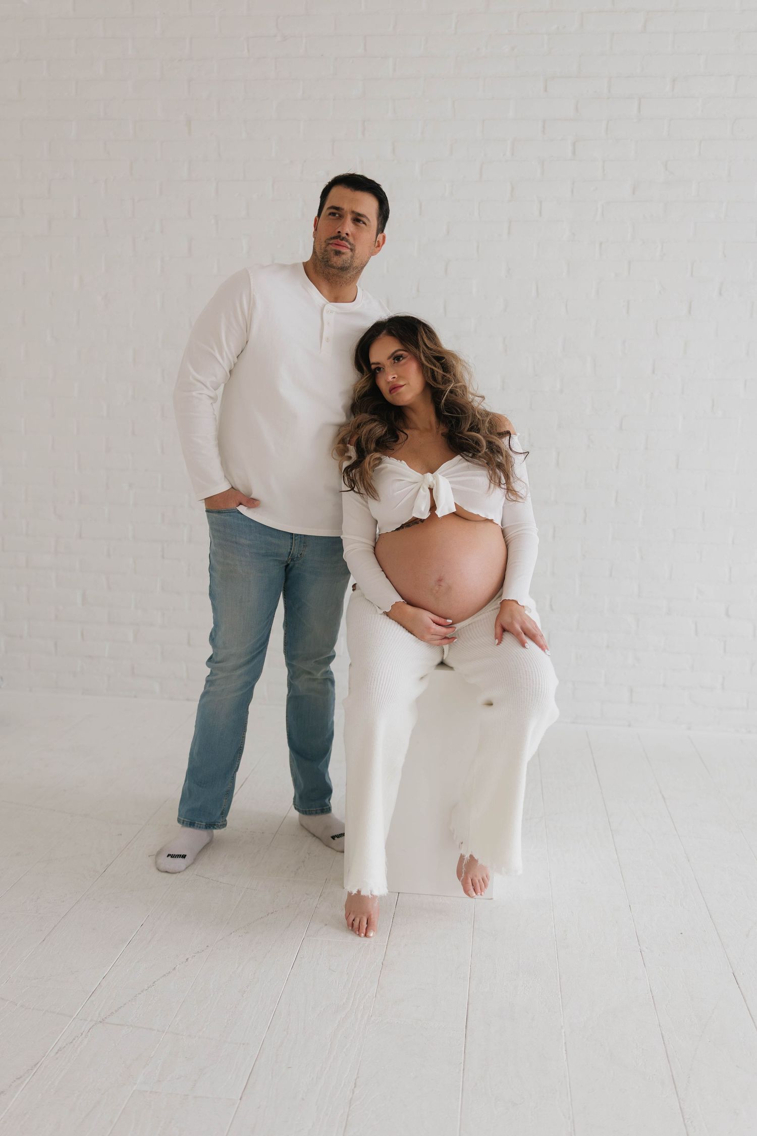 A minimalist maternity photo session showing a couple in white outfits against a light backdrop.