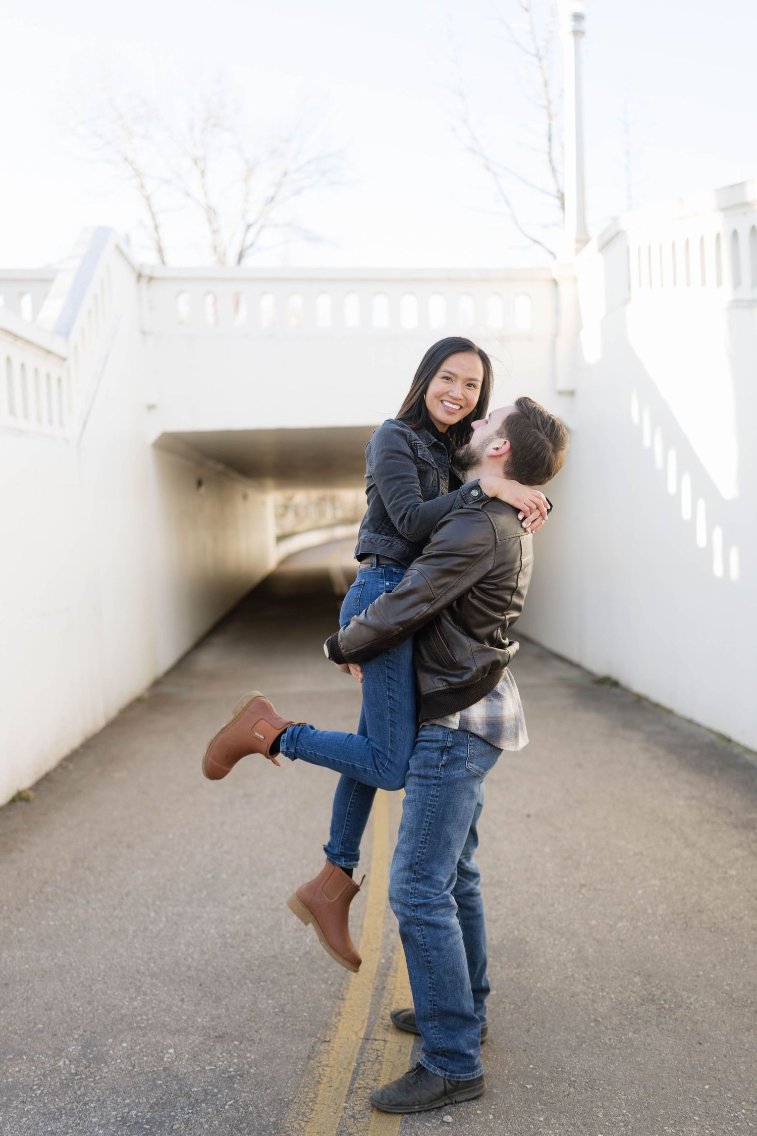 A couple shares a joyful embrace in a white tunnel walkway, with one person lifted off the ground.