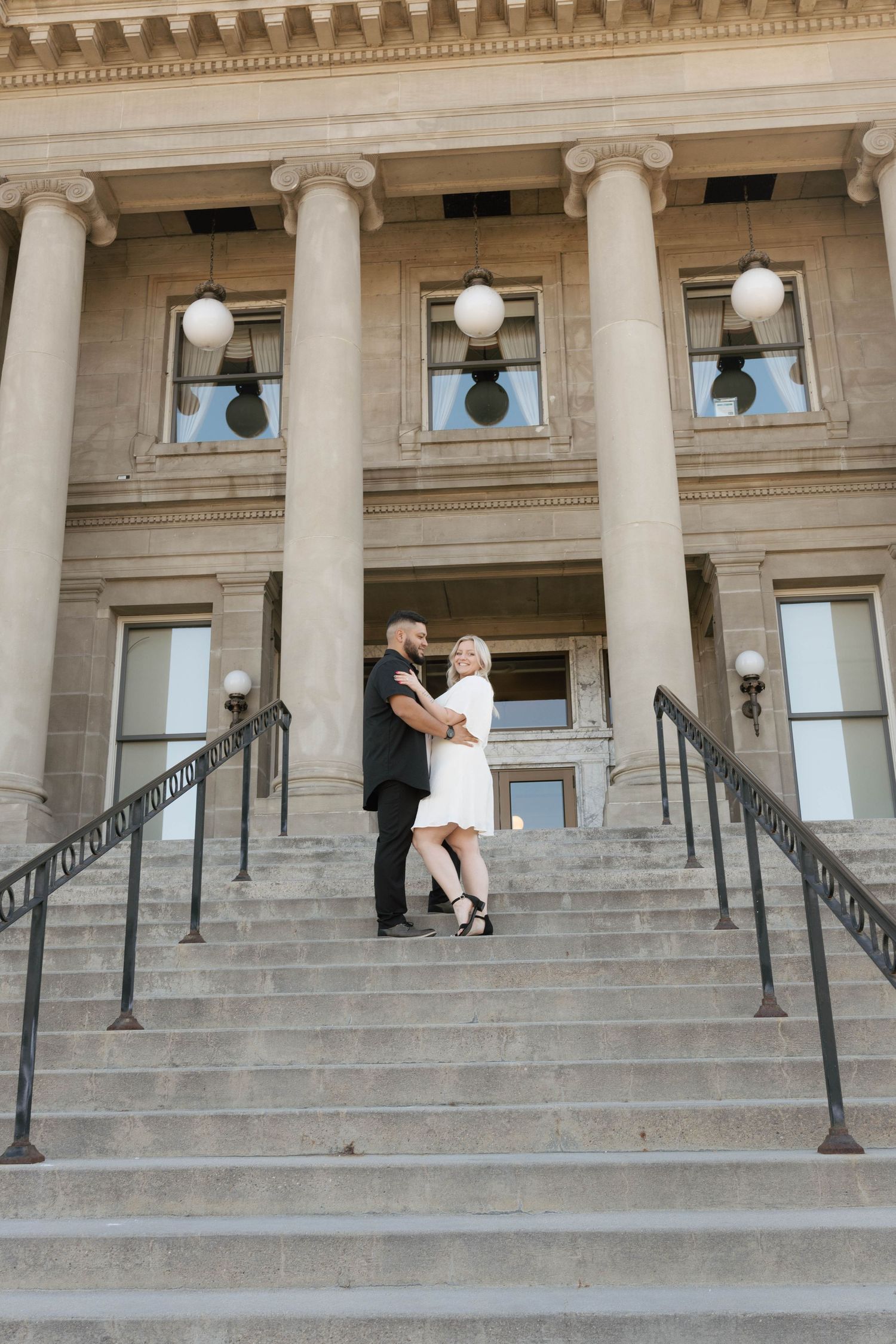 A couple poses on grand stone steps with classical columns of a historic building in three sequential photos.