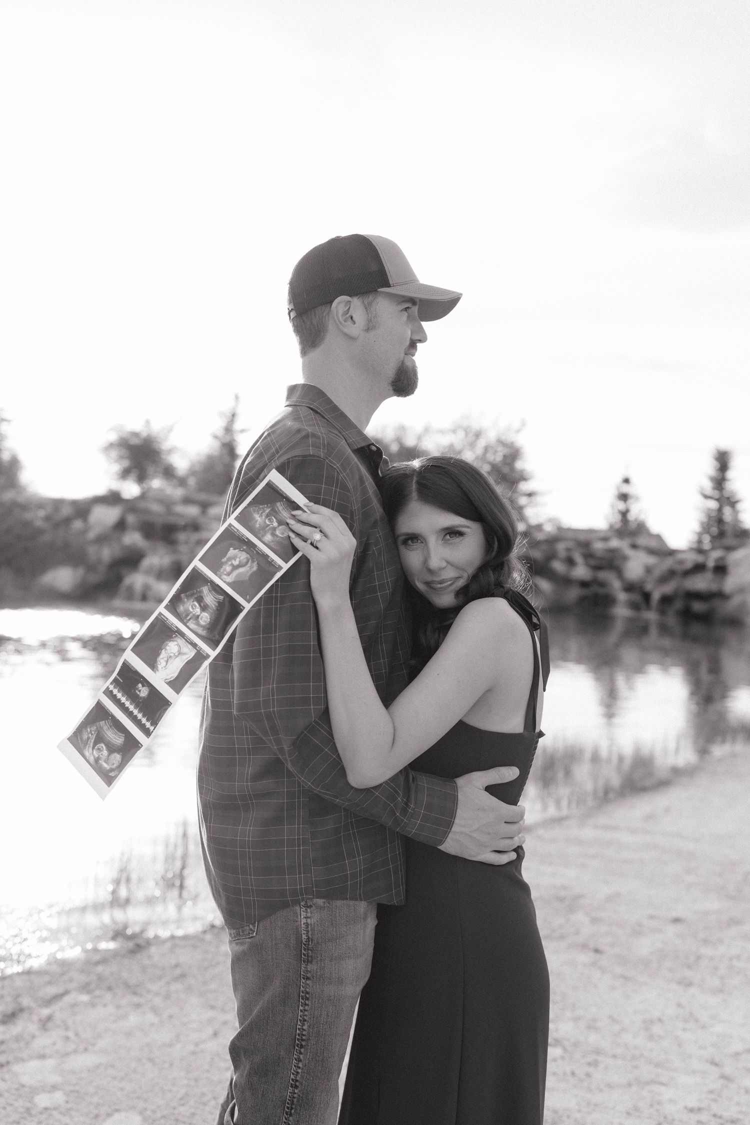 Black and white romantic photoshoot by a lake showing a couple embracing in multiple poses.