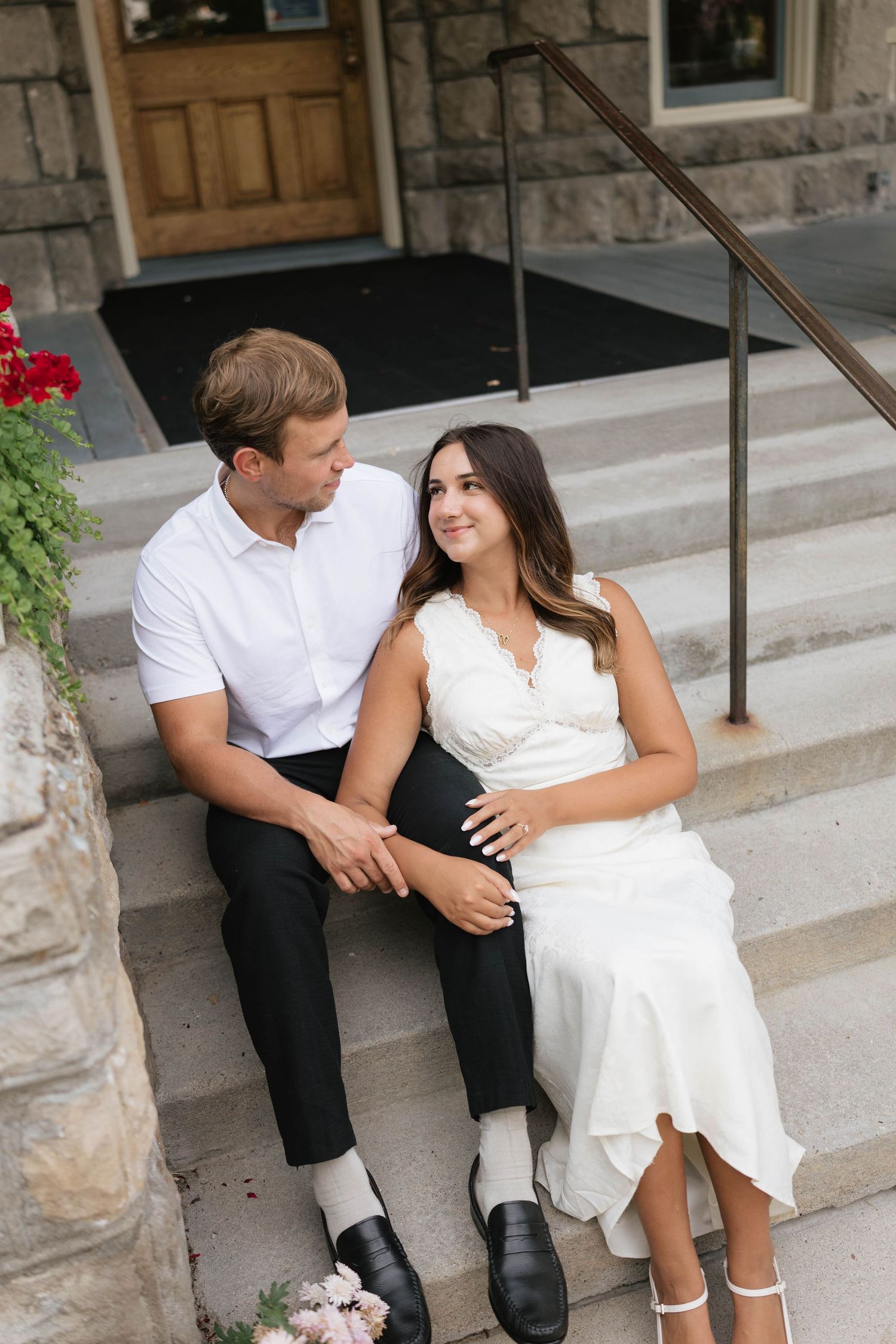 Couple in wedding attire sitting on stone steps of a historic building, sharing a tender moment.