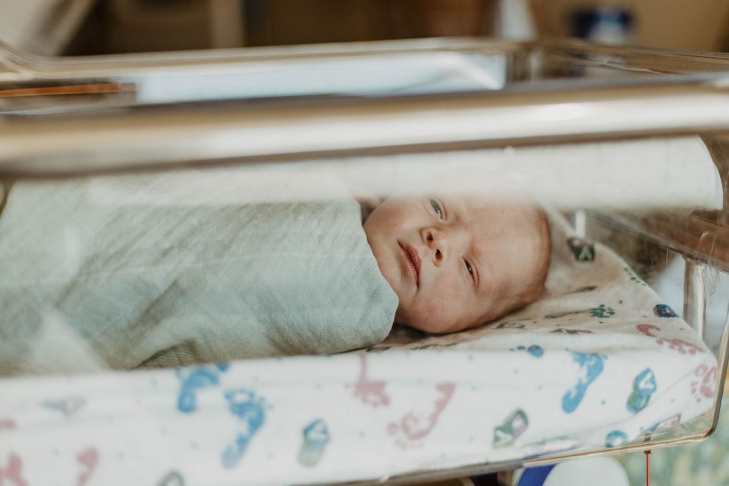 Newborn baby sleeping peacefully in hospital bassinet with patterned blanket.