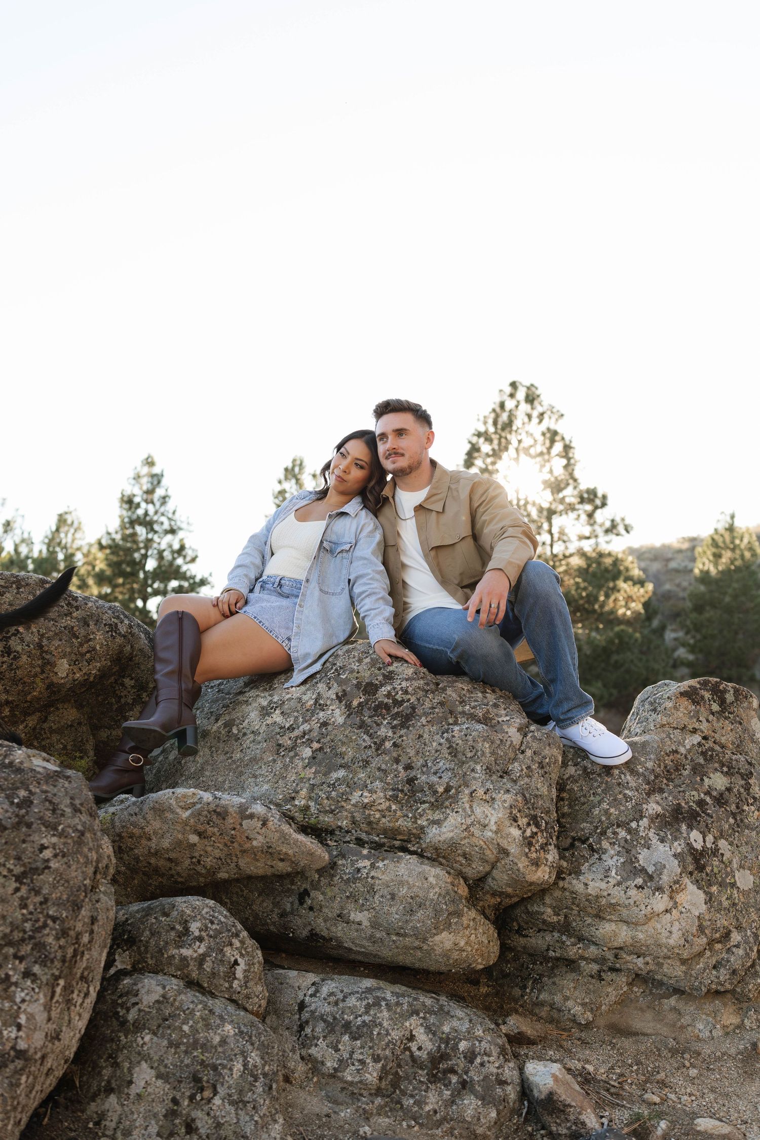 A couple sits together on a rocky outcrop during a sunset photoshoot in a natural outdoor setting.