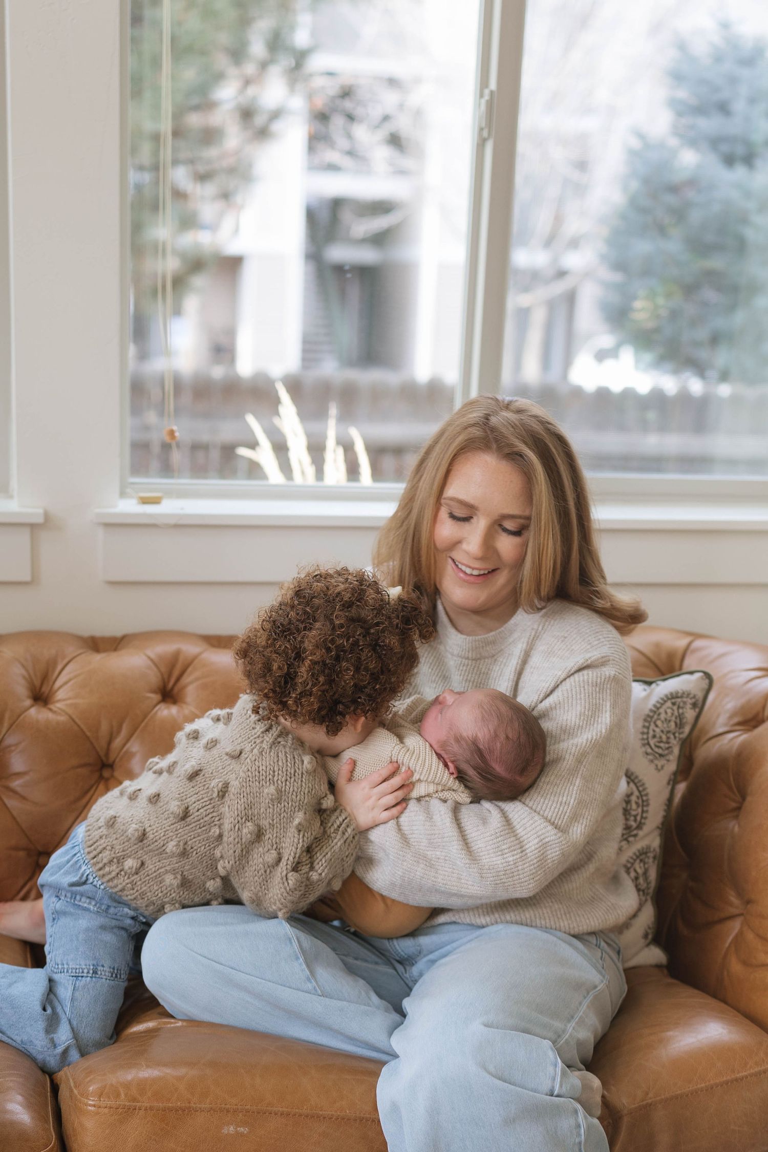 Three connected photos show tender moments shared on a brown leather couch by a window on a bright day.