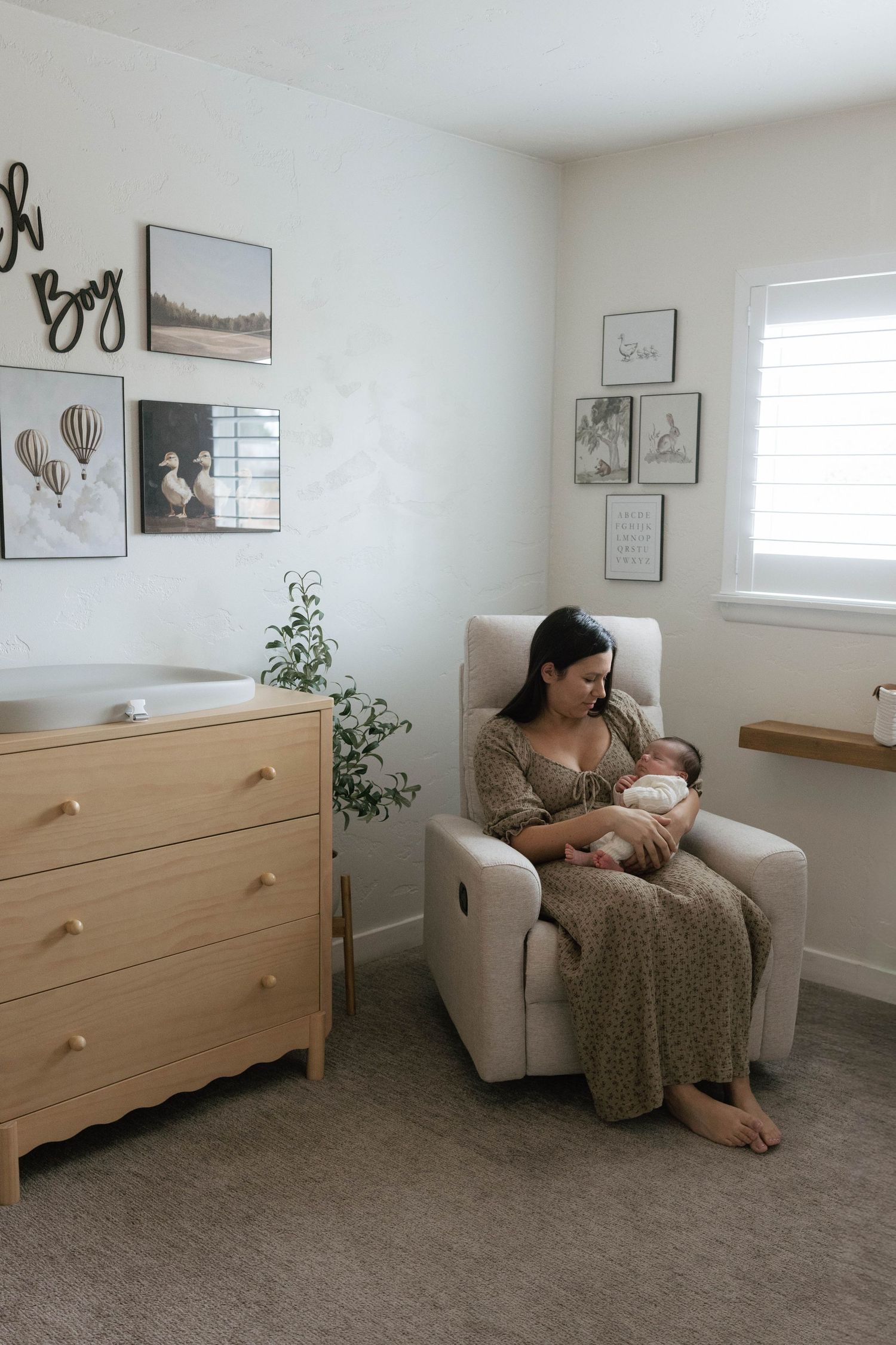 Minimalist nursery corner with wooden dresser, rocking chair, and wall art featuring hot air balloons and nature scenes.